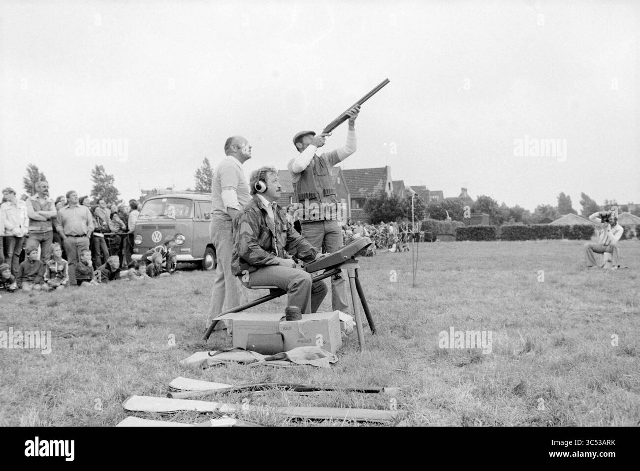 Skeet Shooting, 00-00-1978 Whizgle News, Dutch Desk, Paesi Bassi, 1950-2000 Un gruppo di spettatori guarda con attenzione come due persone partecipano a un concorso di tiro, con una persona che punta un fucile mentre l'altra si prepara al loro turno. Sullo sfondo, un furgone vintage e una folla di spettatori si aggiungono all'atmosfera vivace dell'evento. Foto Stock