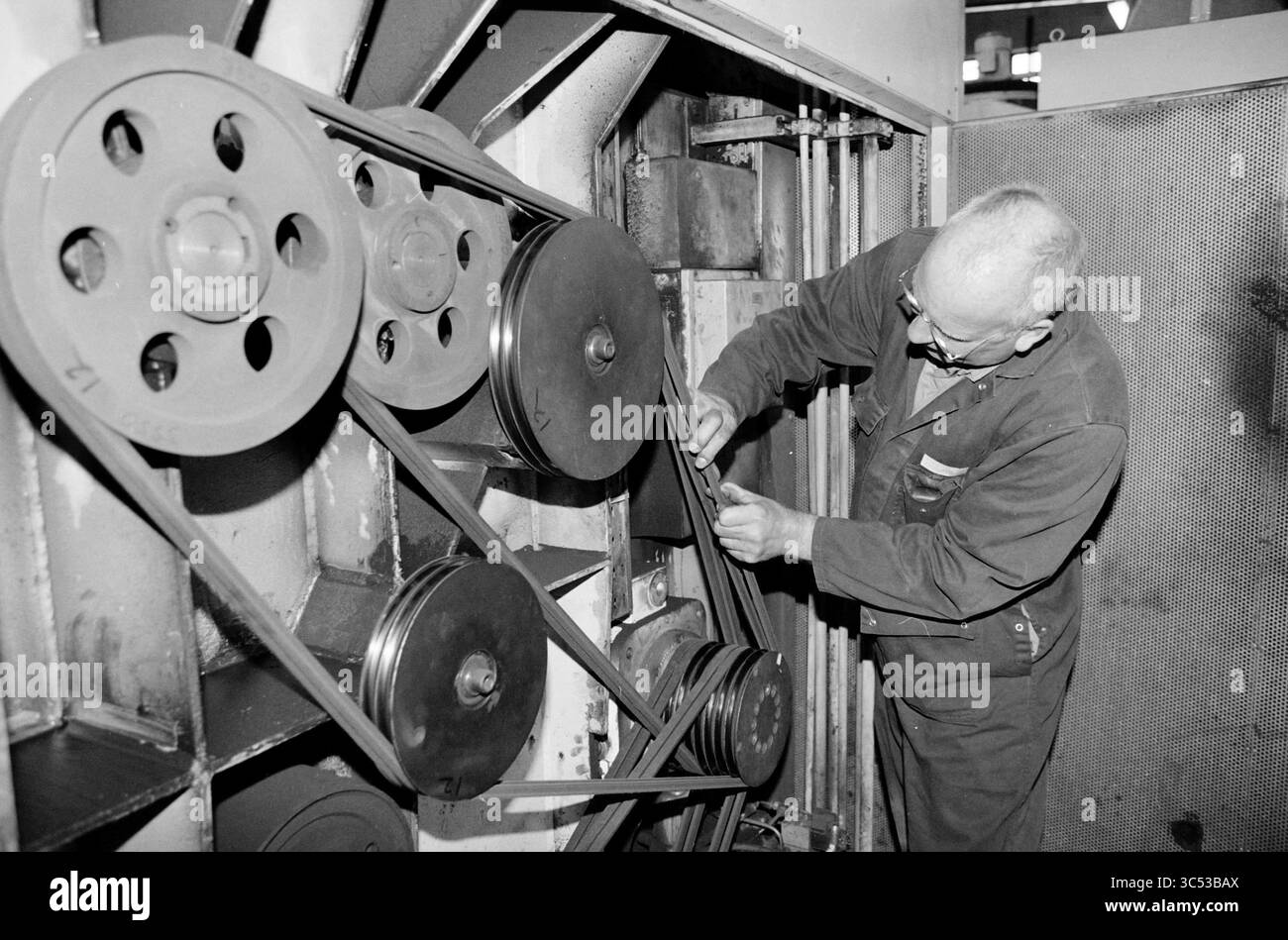 Ned Train: TD in azione, 28-05-2002 Whizgle News, Dutch Desk, Paesi Bassi, 1950-2000 Un tecnico lavora diligentemente su una complessa configurazione di macchinari, regolando pulegge e cinghie per garantire un funzionamento regolare. L'ambiente riflette un ambiente industriale vivace, che mostra la meticolosa attenzione ai dettagli richiesta nelle attività di manutenzione. Foto Stock