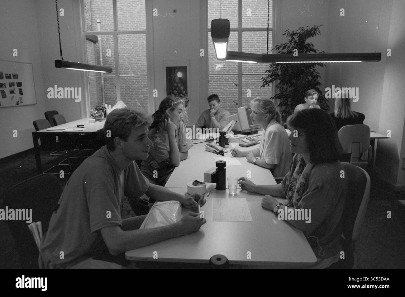 Registrazione per l'agenzia di lavoro studentesca, 02-09-1991 Whizgle News, Dutch Desk, Paesi Bassi, 1950-2000 Un gruppo di studenti si impegna in discussione e collaborazione su un lungo tavolo, circondato da illuminazione moderna e grandi finestre. Alcuni sono concentrati su note e materiali, mentre altri condividono idee in piccoli gruppi, creando un'atmosfera vivace di apprendimento e lavoro di squadra. Foto Stock