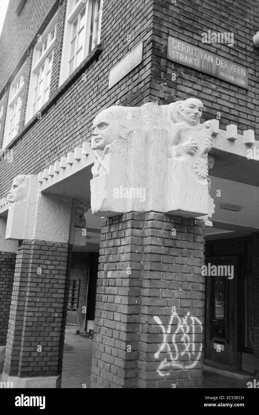 Rep. Amsterdam, Villages and Cities, Amsterdam, Paesi Bassi, 13-03-1984 Whizgle News, Dutch Desk, Paesi Bassi, 1950-2000 l'angolo di un edificio in mattoni presenta intricate sculture in pietra intagliate che raffigurano figure umane, aggiungendo un tocco artistico unico all'architettura. I graffiti possono essere visti sul muro, in contrasto con i dettagli in pietra, mentre un cartello stradale con la scritta "GERRIT VAN DER VEEN STRAAT" indica la posizione. Foto Stock