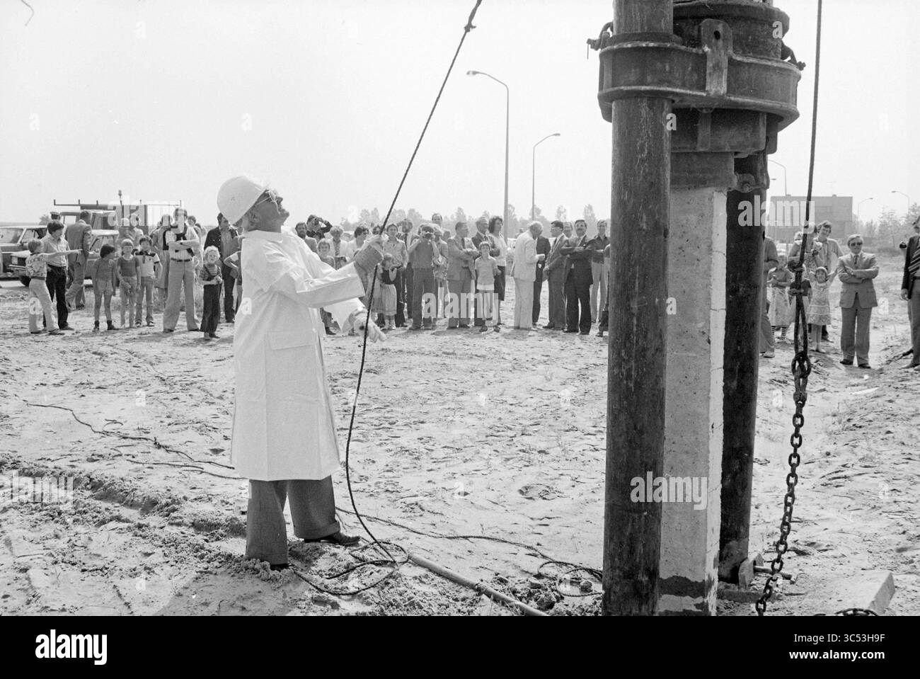 Primo mucchio di case Spaarndam est, primo mucchio, Spaarndam, 19-06-1979 Whizgle News, Dutch Desk, paesi Bassi, 1950-2000 Un gruppo di osservatori si riunisce intorno a un cantiere come operaio in un camice da laboratorio che gestisce macchinari, dimostrando un processo di perforazione o scavo. La scena cattura l'attenzione della folla, illustrando un momento di coinvolgimento pubblico nell'attività industriale. Foto Stock