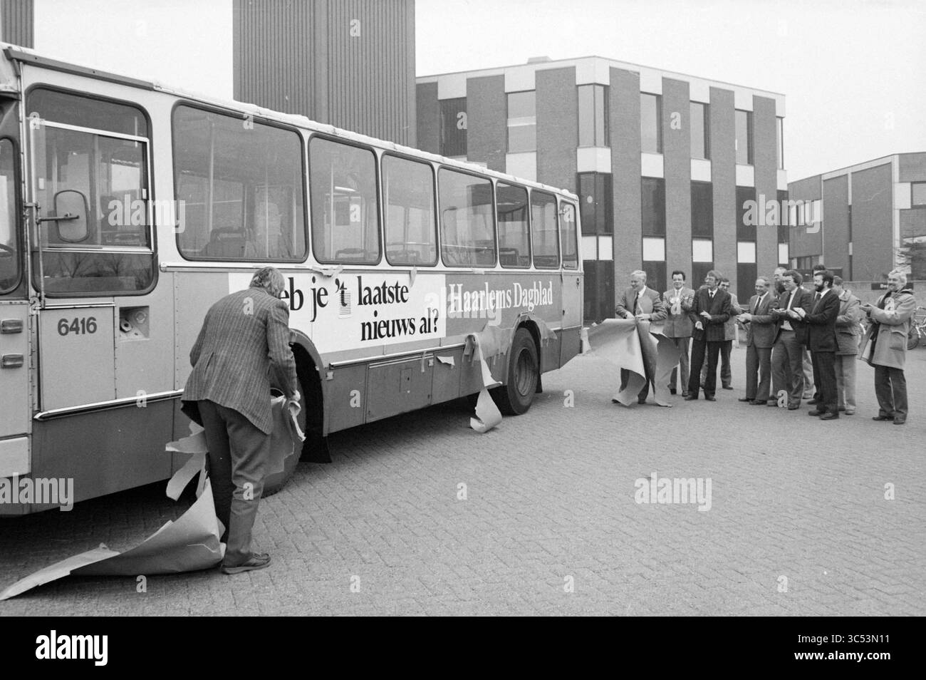 Annuncio pubblicitario Haarlems Dagblad su autobus NZH, 17-03-1986 Whizgle News, Dutch Desk, Paesi Bassi, 1950-2000 Un gruppo di uomini si riunisce intorno a un autobus mentre una persona scopre la pubblicità sul suo lato, rivelando un messaggio che chiede se lo spettatore ha sentito le ultime notizie. L'ambientazione presenta edifici moderni sullo sfondo, creando uno sfondo per questo momento di pubblico impegno. Foto Stock