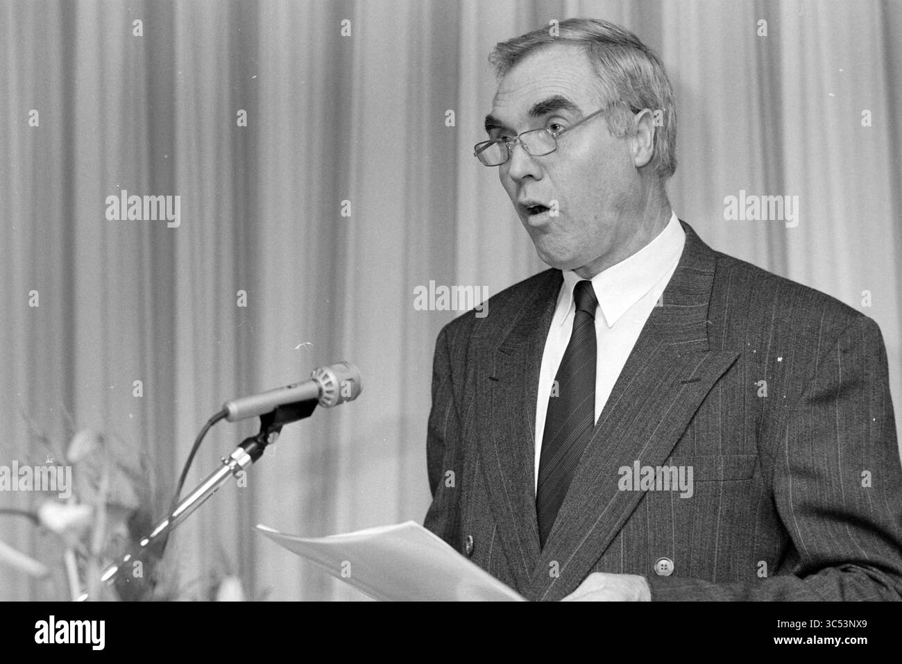 Relatore Sig. Santwijk, Hillegom, 06-12-1992 Whizgle News, Dutch Desk, Paesi Bassi, 1950-2000 Un uomo in tuta sta davanti ad un microfono, pronuncia con passione un discorso, con gli occhi larghi e la bocca aperta nell'espressione. Tiene un foglio di carta in una mano mentre si trova davanti a una tenda avvolta dietro di lui. Foto Stock