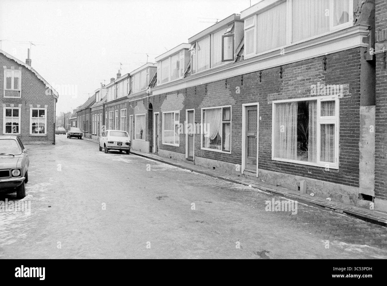 Fila esterna di immobili in affitto mal mantenuti, 22-01-1979 Whizgle News, Dutch Desk, Paesi Bassi, 1950-2000 Una strada tranquilla fiancheggiata da modeste case in mattoni, con grandi finestre rivestite di tende trasparenti. Un'auto parcheggiata è visibile lungo la strada e la scena trasmette un senso di calma, con un pizzico di nostalgia nell'architettura e nell'atmosfera. Foto Stock