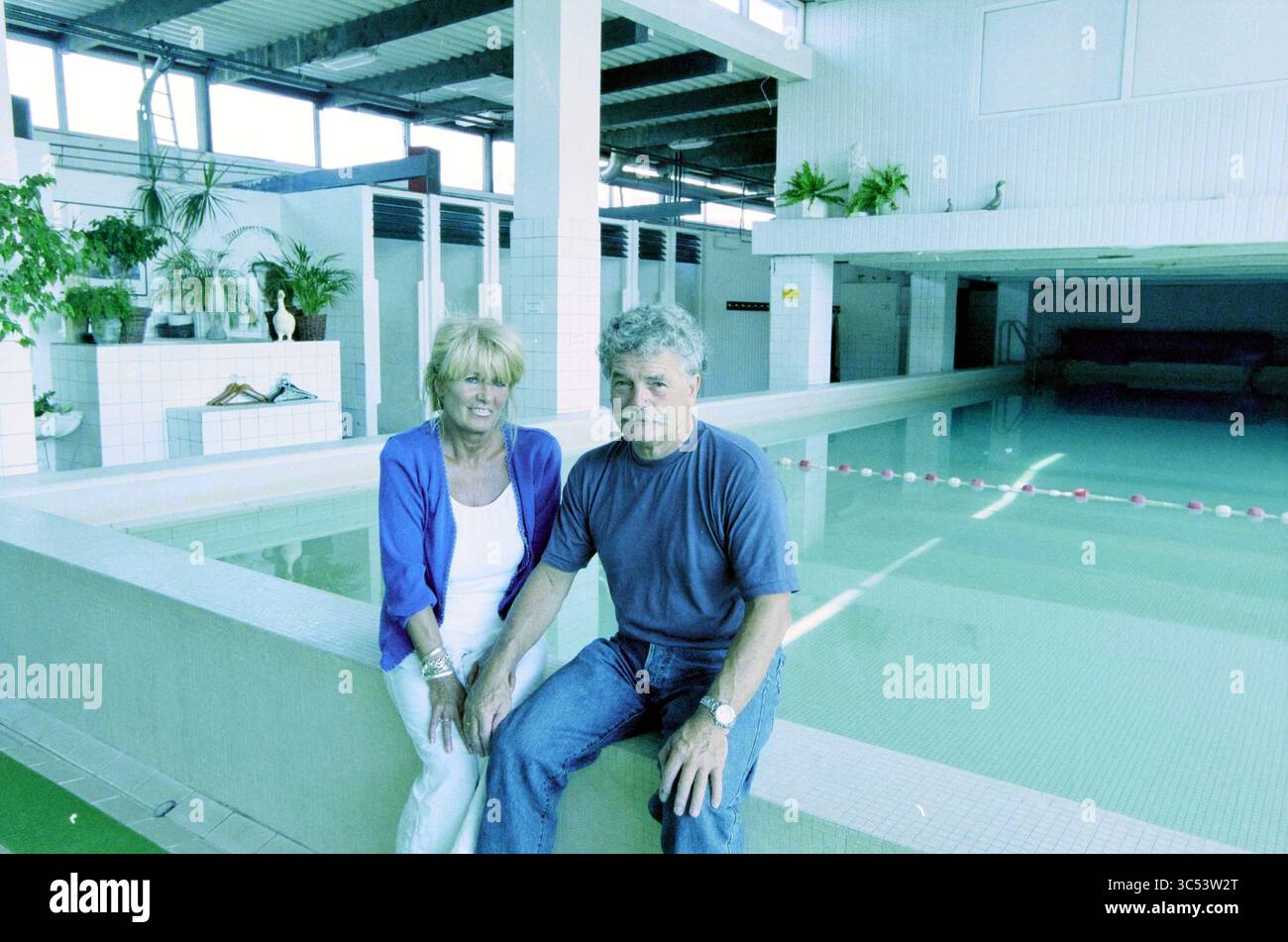 Fiona Sonneveld in piscina, 28-08-2002 Whizgle News, Dutch Desk, The Netherlands, 1950-2000 Una coppia siede al bordo di una piscina, circondato da uno spazioso ambiente interno caratterizzato da piante e pareti piastrellate. L'atmosfera sembra rilassata, con la luce che si riflette sulla superficie dell'acqua. Foto Stock