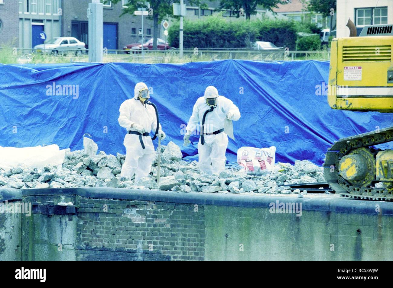Amianto a Zuidersluis, IJmuiden, IJmuiden, Paesi Bassi, 26-07-1999 Whizgle News, Dutch Desk, Paesi Bassi, 1950-2000 due persone in tuta protettiva stanno navigando in un cantiere roccioso, mentre un macchinario giallo si trova nelle vicinanze e un telone blu copre parte dell'area. Foto Stock