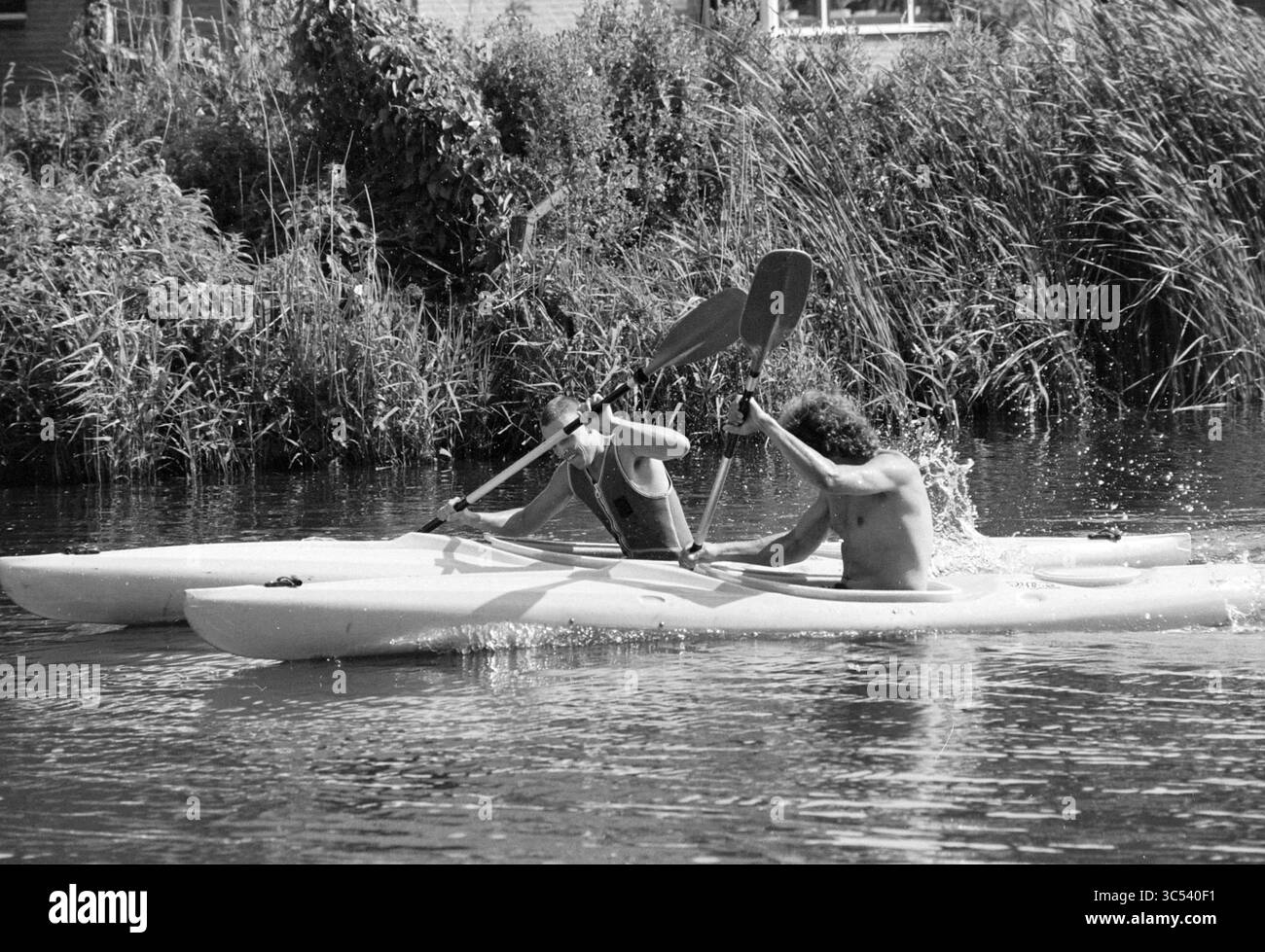 Gare di canoa, Spaarneschool Spaarndam, Spaarndam, 03-07-1992 Whizgle News, Dutch Desk, i Paesi Bassi, 1950-2000 due persone pagaiano vigorosamente in kayak separati, creando spruzzi in acqua mentre navigano in un fiume tranquillo fiancheggiato da una vegetazione lussureggiante. Foto Stock