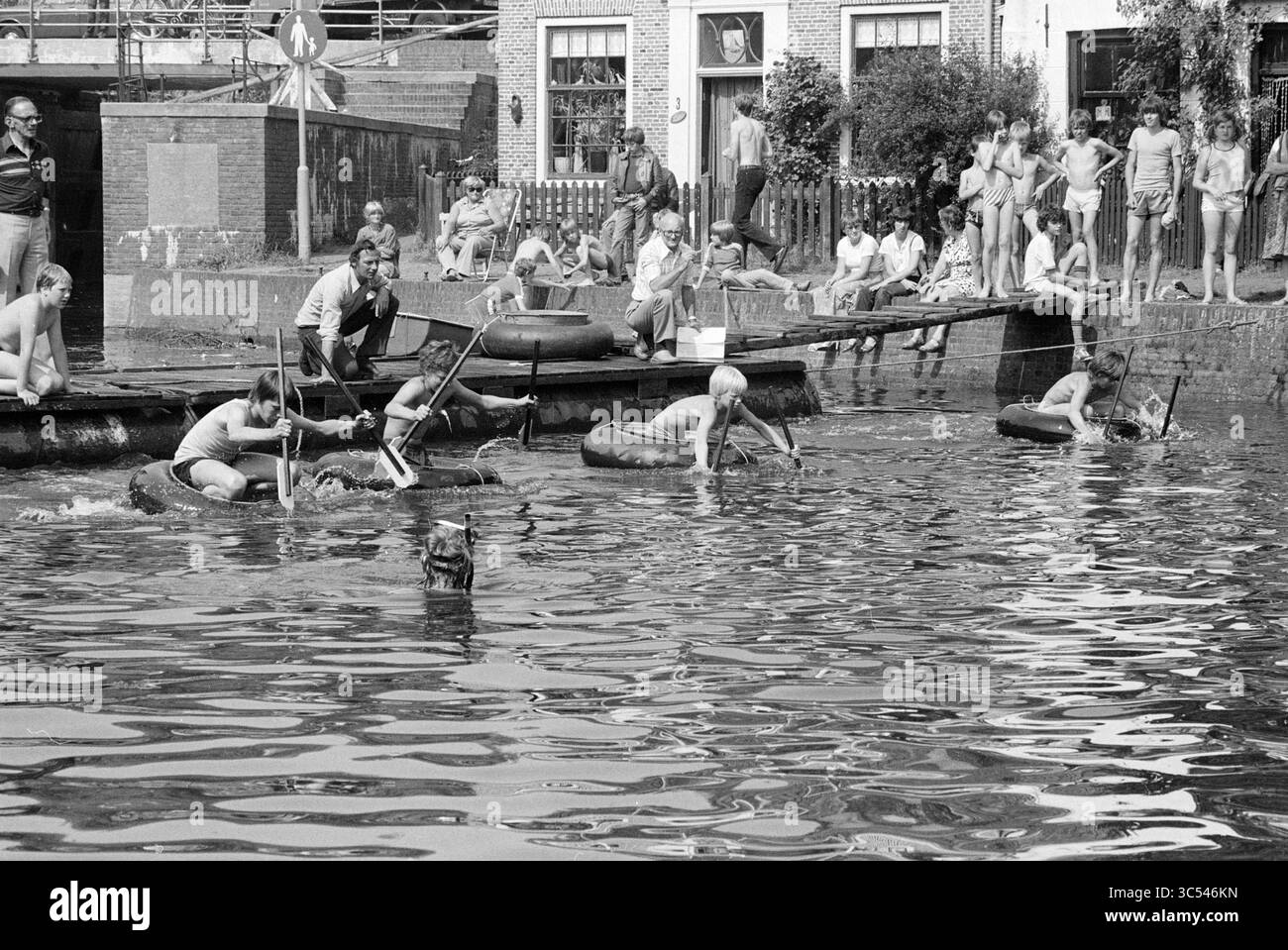Escursioni in barca con vasca e cuscino Fight Spaarndam, Spaarndam, Spaarndam, 23-06-1979 Whizgle News, Dutch Desk, i Paesi Bassi, 1950-2000 Una vivace scena in riva all'acqua presenta bambini che giocano e si divertono, alcuni galleggiano su camere d'aria mentre altri sono impegnati in varie attività lungo le rive. Nelle vicinanze, un gruppo di spettatori guarda il divertimento, creando una miscela di eccitazione e spirito comunitario. Foto Stock