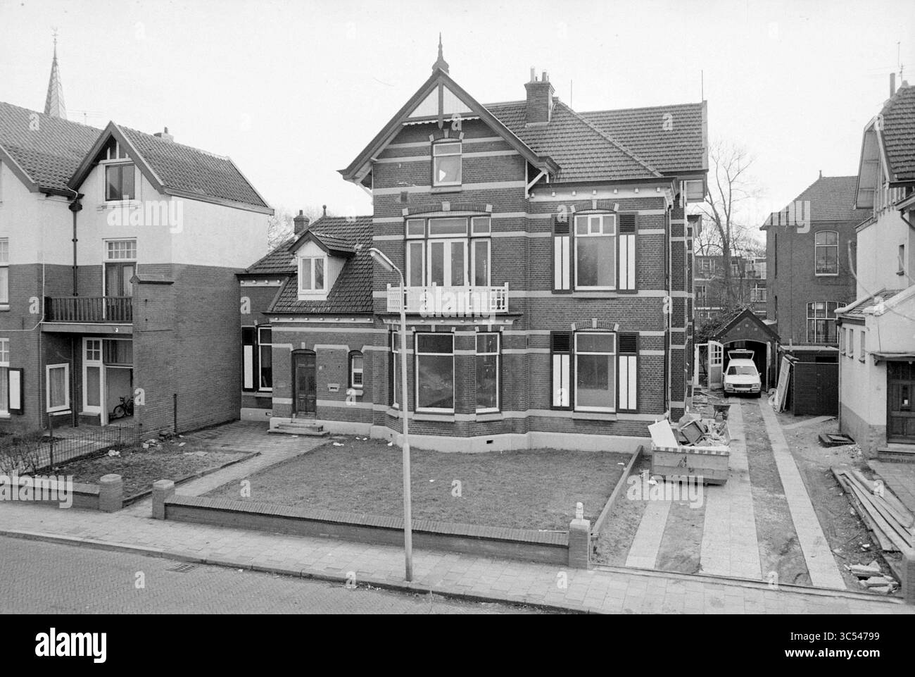 Esterno del vecchio edificio Schippersbeurs, IJm., esterno, 11-02-1977 Whizgle News, Dutch Desk, i Paesi Bassi, 1950-2000 Una grande e distintiva casa in mattoni caratterizzata da dettagli architettonici ornati, tra cui un balcone e finestre multiple, sorge in una zona residenziale. Il cantiere sembra ben mantenuto, con materiali da costruzione visibili, a indicare i lavori in corso nelle vicinanze. Le case circostanti riflettono un mix di stili, contribuendo al carattere del quartiere. Foto Stock