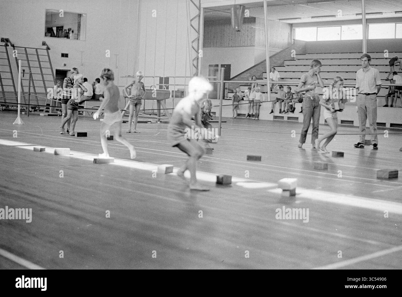 Sports Day Nieuw Vennep, Sports and Sports Week, 05-08-1970 Whizgle News, Dutch Desk, Paesi Bassi, 1950-2000 Una vivace scena di palestra dove i bambini sono impegnati in varie attività, navigando sugli ostacoli mentre gli adulti osservano nelle vicinanze. L'atmosfera è piena di energia poiché i partecipanti si concentrano sull'equilibrio e il coordinamento. Foto Stock