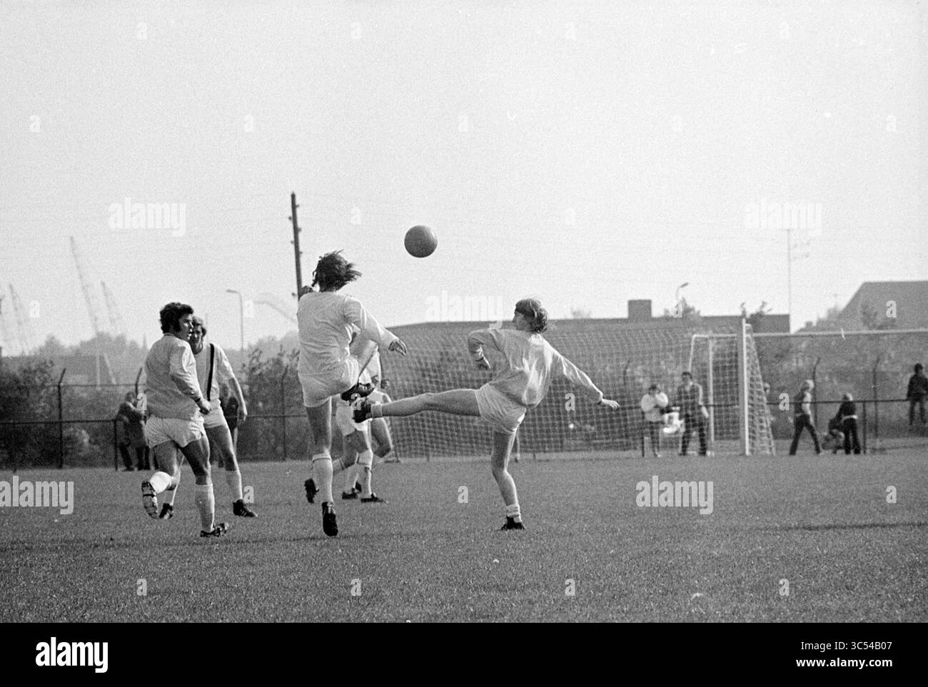 Partita di calcio Whizgle News, Dutch Desk, Paesi Bassi, 1950-2000 Un gruppo di giovani atleti partecipa a una vivace partita di calcio, mostrando movimenti dinamici in cui un giocatore tenta abilmente di calciare la palla mentre altri si posizionano in attesa del gioco. L'energia vibrante del gioco è palpabile, con gli spettatori sullo sfondo che si aggiungono all'atmosfera della competizione e del lavoro di squadra. Foto Stock