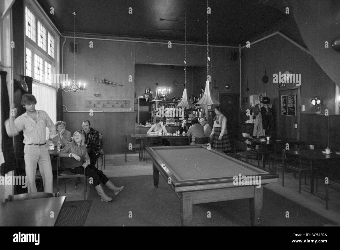 Quartiere in mostra, Frans Halsbuurt, People in a café biliardo, Haarlem, Paesi Bassi, 08-12-1980 Whizgle News, Dutch Desk, i Paesi Bassi, 1950-2000 Un ambiente vivace in un bar accogliente, con vari clienti impegnati in conversazione e attività ricreative. Un tavolo da biliardo occupa un posto centrale, mentre un gruppo di amici si rilassa a un tavolo vicino. L'atmosfera sfoggia un mix di interazione sociale informale e arredamento vintage. Foto Stock