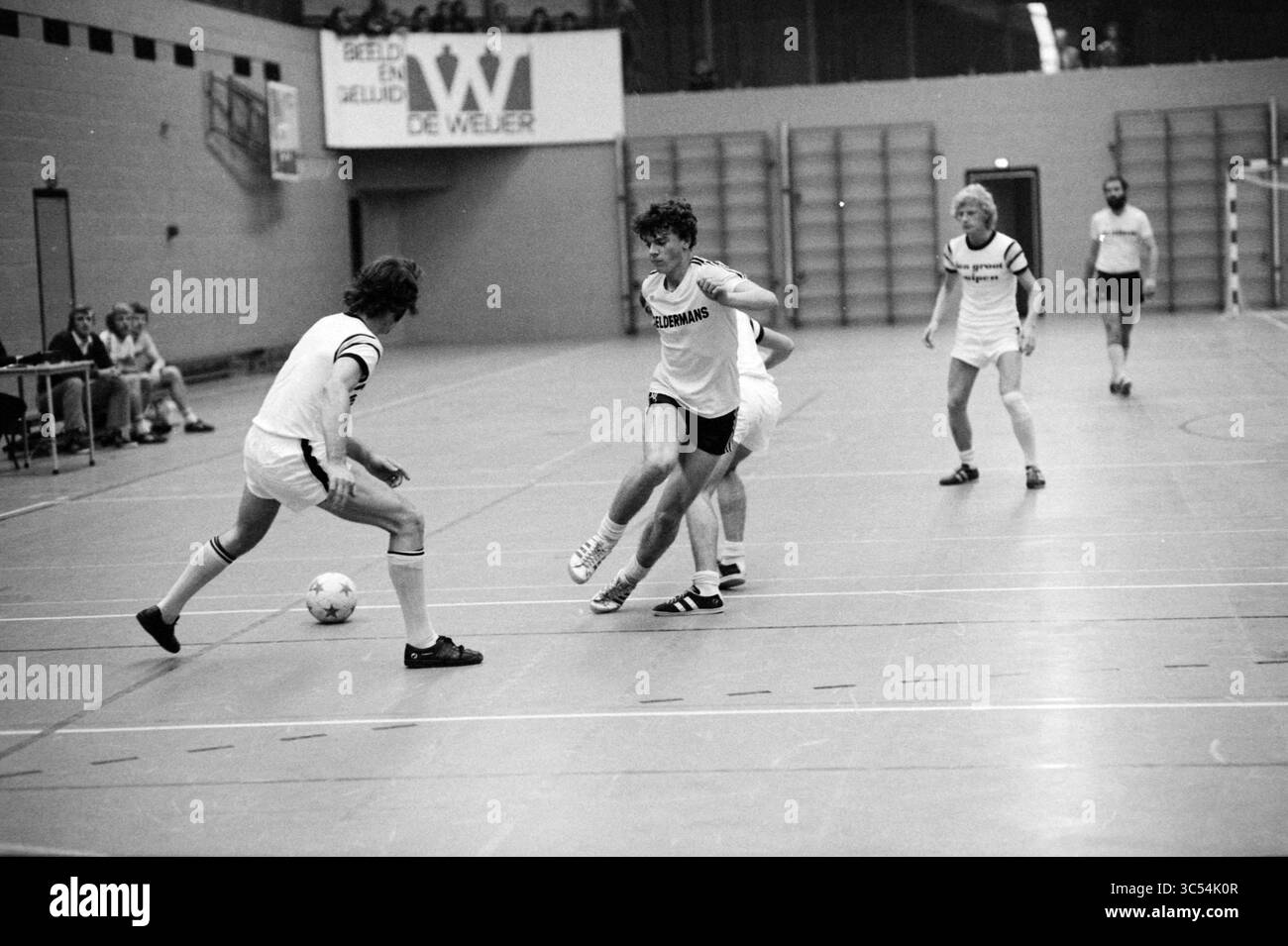 Huiben - Geldermans, calcio, 02-10-1978 Whizgle News, Dutch Desk, Paesi Bassi, 1950-2000 Una dinamica partita di calcio al coperto in corso, in cui i giocatori mettono in mostra le loro abilità mentre manovrano la palla e sfuggono agli avversari. Le espressioni mirate e le posizioni atletiche mettono in risalto lo spirito competitivo del gioco. Gli spettatori sullo sfondo guardano intensamente dai loro posti a sedere. Foto Stock
