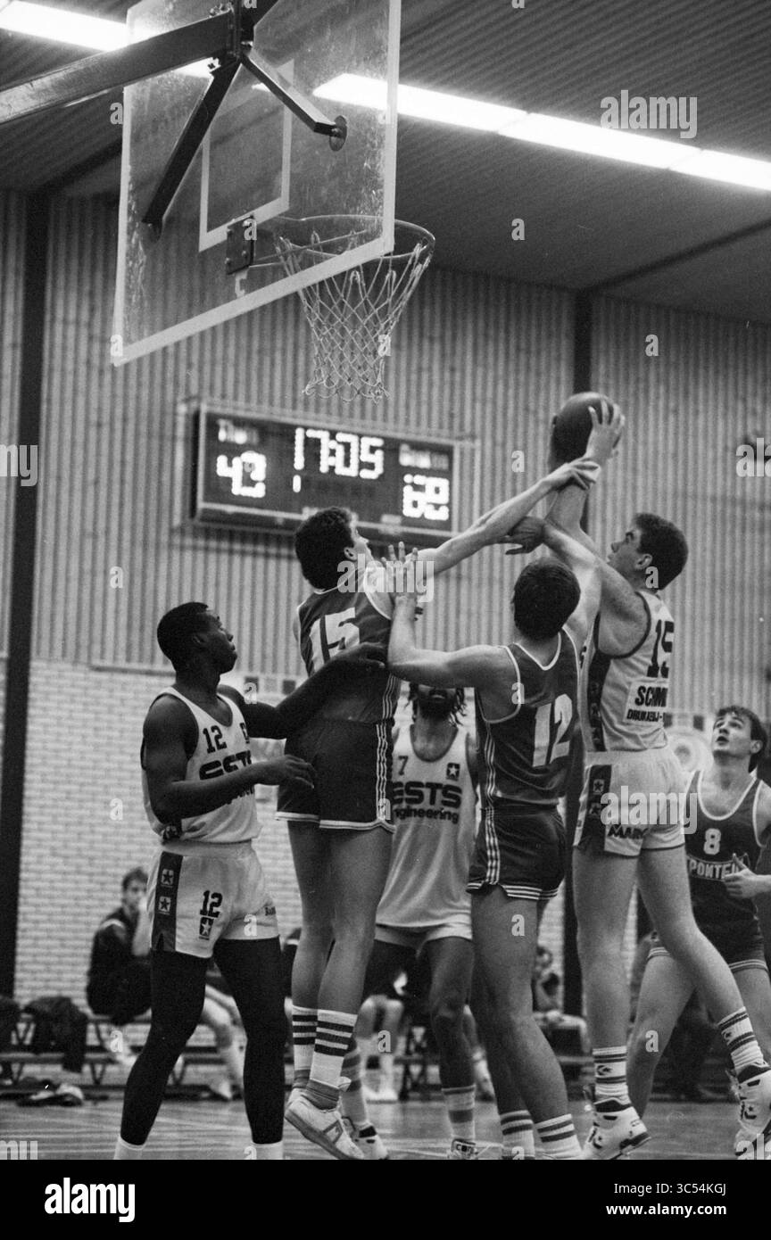 Basket Whizgle News, Dutch Desk, Paesi Bassi, 1950-2000 Un momento di tensione in una partita di basket, in cui i giocatori di entrambe le squadre si sfidano per il possesso della palla vicino al cerchio, mostrando un intenso atletismo e un lavoro di squadra. Il tabellone segnapunti indica una partita ravvicinata con poco meno di 18 minuti rimasti nel gioco. Foto Stock