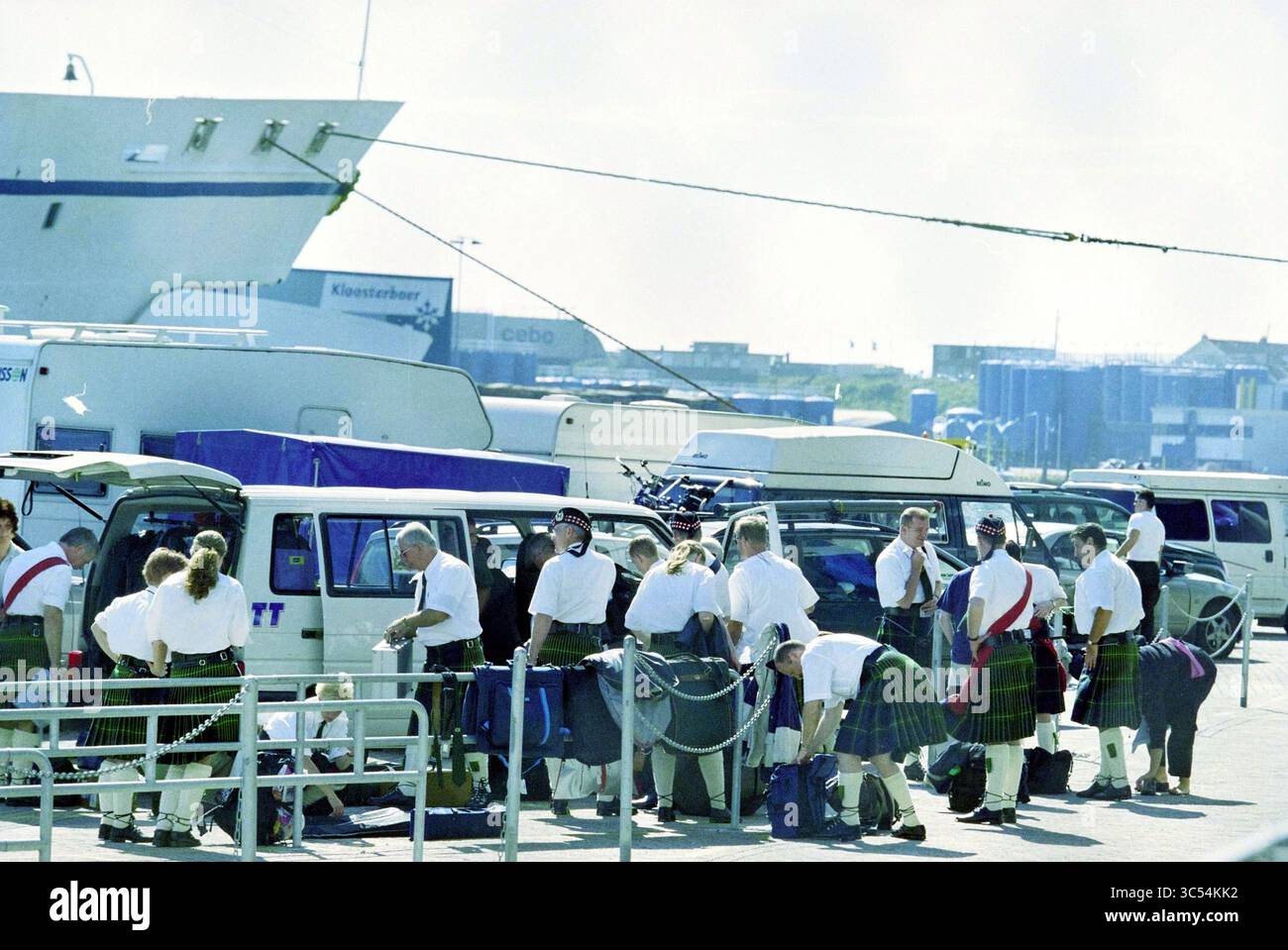 Schotten Harbour IJmuiden, IJmuiden, Paesi Bassi, 01-08-2000 Whizgle News, Dutch Desk, i Paesi Bassi, 1950-2000 Un gruppo di persone in kilt tradizionali si riunisce vicino ai veicoli in un porto affollato, preparandosi per un evento o una performance, mentre una grande nave incombe sullo sfondo. Foto Stock