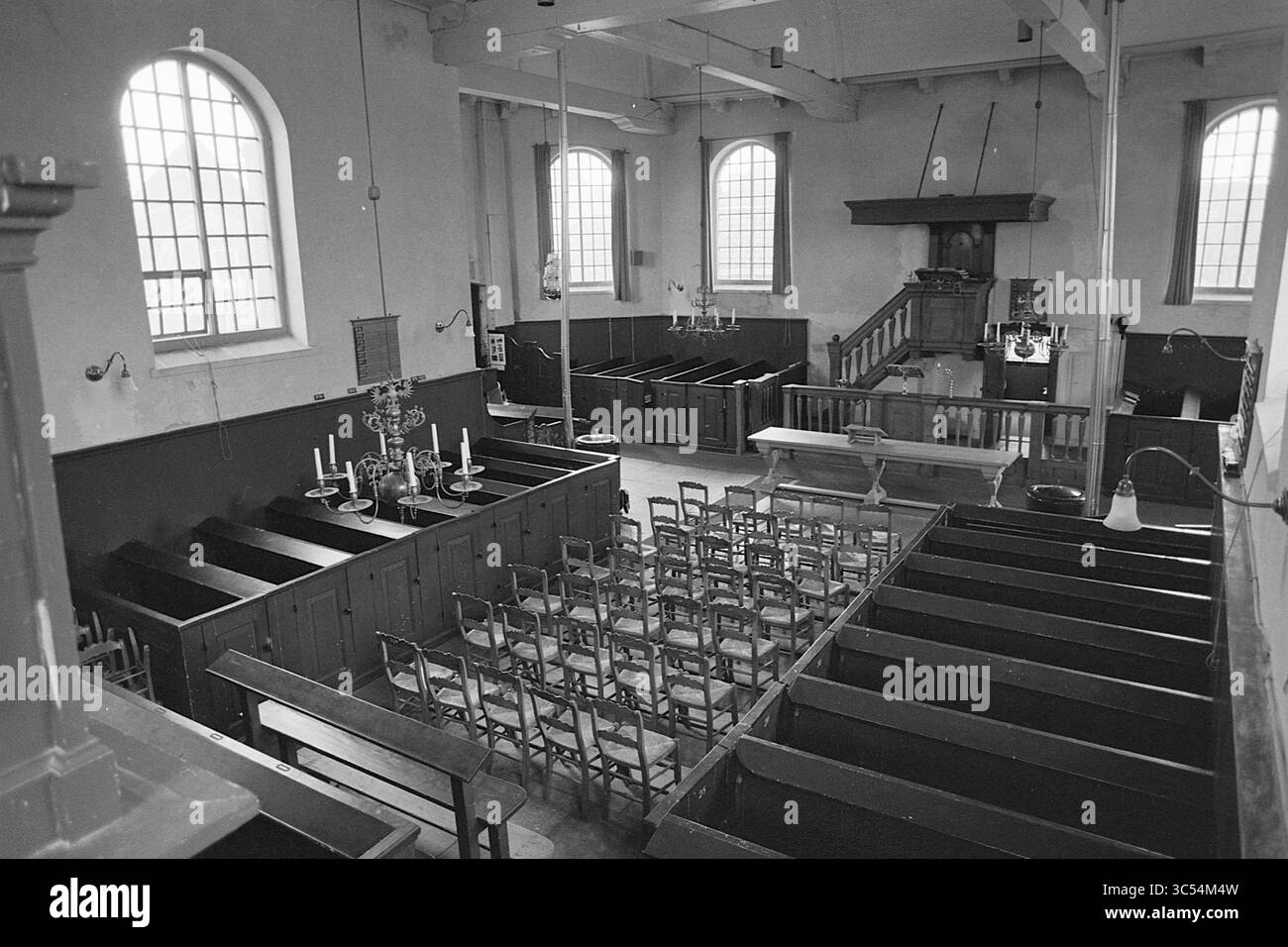 Report Vecchia Chiesa di Spaarndam, Chiese, Report, Spaarndam, Kerkplein, 15-03-1977 Whizgle News, Dutch Desk, Paesi Bassi, 1950-2000 una vista interna di una cappella storica con pali di legno disposti per la congregazione, con grandi finestre che consentono la luce naturale a riempire lo spazio. Il pulpito si erge davanti, accompagnato da elementi decorativi come candelabri e lampade a sospensione, creando un'atmosfera serena e invitante. Foto Stock Report Vecchia Chiesa di Spaarndam, Chiese, Report, Spaarndam, Kerkplein, 15-03-1977 Whizgle News, Dutch Desk, Paesi Bassi, 1950-2000 una vista interna di una cappella storica con pali di legno disposti per la congregazione, con grandi finestre che consentono la luce naturale a riempire lo spazio. Il pulpito si erge davanti, accompagnato da elementi decorativi come candelabri e lampade a sospensione, creando un'atmosfera serena e invitante. Foto Stock