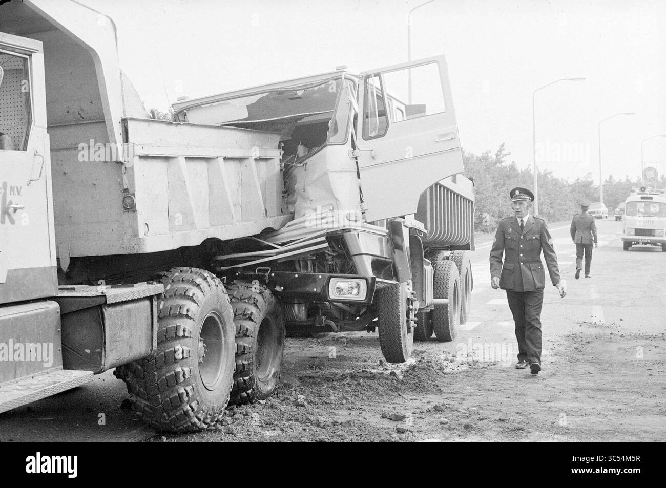 2 camion su Rijksweg 9 a Beverwijk, incidenti, collisioni, incidenti, 25-06-1974 Whizgle News, Dutch Desk, Paesi Bassi, 1950-2000 Un agente di polizia ispeziona una scena di collisione, dove due camion sono entrati in collisione, uno in parte si è schiantato contro l'altro. L'area sembra essere oggetto di indagine, con un'altra cifra sullo sfondo che valuta il danno. Foto Stock
