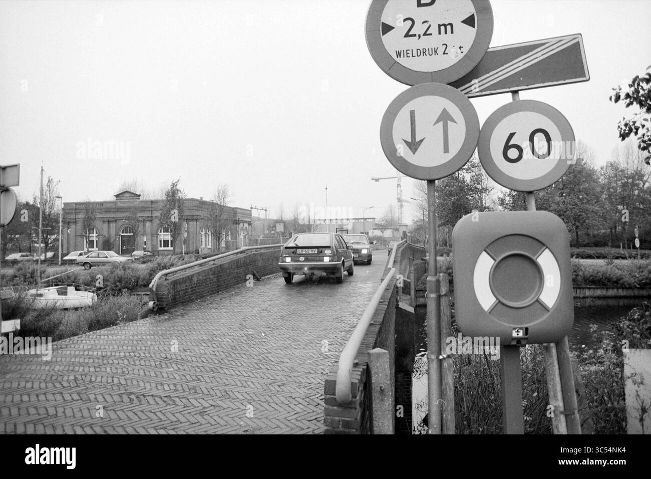 Amstel Bridge, Heemstede, Heemstede, Paesi Bassi, 04-11-1992 Whizgle News, Dutch Desk, Paesi Bassi, 1950-2000 Un'auto attraversa un ponte stretto contrassegnato da vari segnali stradali che indicano limiti di altezza, limiti di velocità e frecce direzionali, mentre un edificio storico e un cantiere sono visibili sullo sfondo in mezzo a cieli sovrastati. Foto Stock