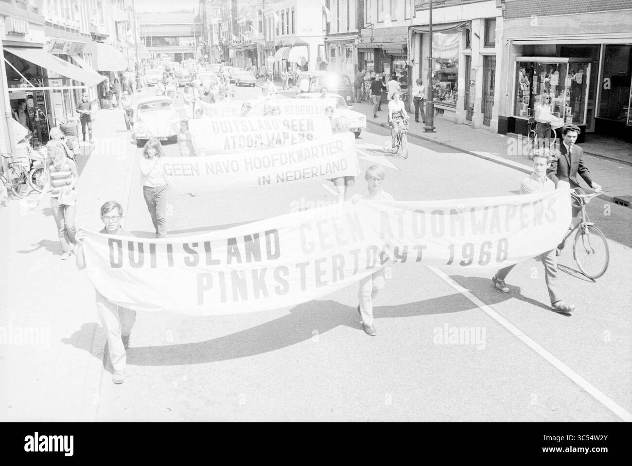 Demonstration in Kruisweg, Demonstration, 01-06-1968 Whizgle News, Dutch Desk, Paesi Bassi, 1950-2000 Un gruppo di manifestanti marcia attraverso una strada trafficata, tenendo in mano grandi striscioni che recitano "Duitsland Geen Atoomwapens" e "Pinksterdicht 1968", che difendono le armi nucleari. Biciclette e veicoli fiancheggiano la strada, evidenziando un periodo di protesta attiva e di impegno pubblico. Foto Stock