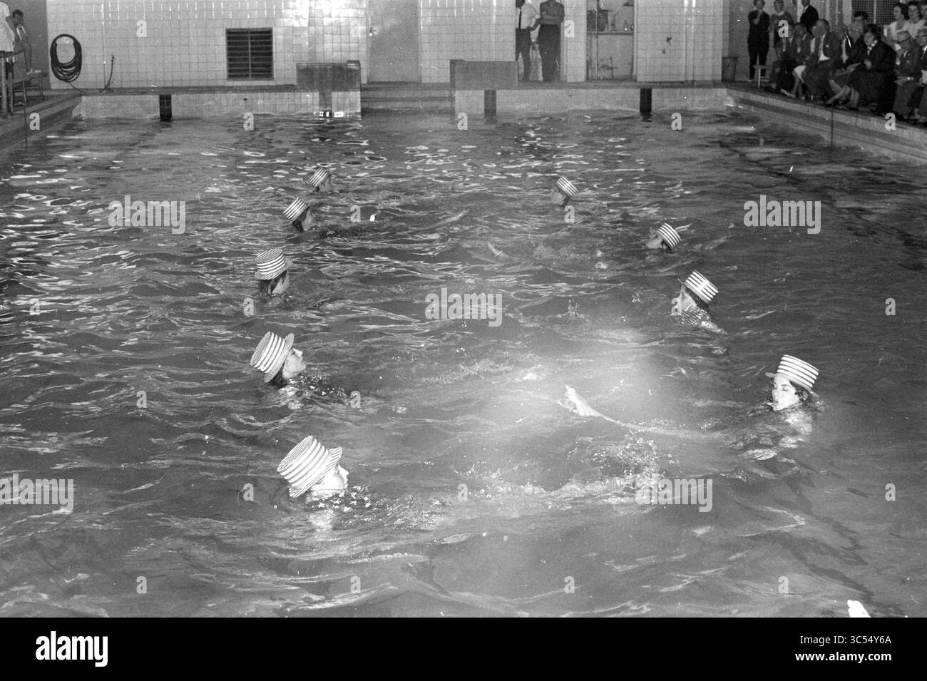 Nuotatori con un pubblico Whizgle News, Dutch Desk, Paesi Bassi, 1950-2000 Uno spettacolo di nuoto sincronizzato con un gruppo di nuotatori che indossano cappelli a righe, che si muovono aggraziatamente all'unisono in una grande piscina mentre il pubblico osserva da bordo campo. Foto Stock