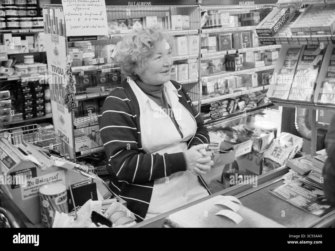 Quartiere da osservare: Oosterwijk, negozi locali, Haarlem, Paesi Bassi, 10-11-1980 Whizgle News, Dutch Desk, Paesi Bassi, 1950-2000 Un negoziante amichevole si trova dietro il bancone, sorridendo mentre interagisce con i clienti. Il minimarket è pieno di vari prodotti, creando un'atmosfera vivace. Gli scaffali riforniti di generi alimentari e articoli per la casa la circondano, mettendo in risalto la natura vivace del negozio. Foto Stock