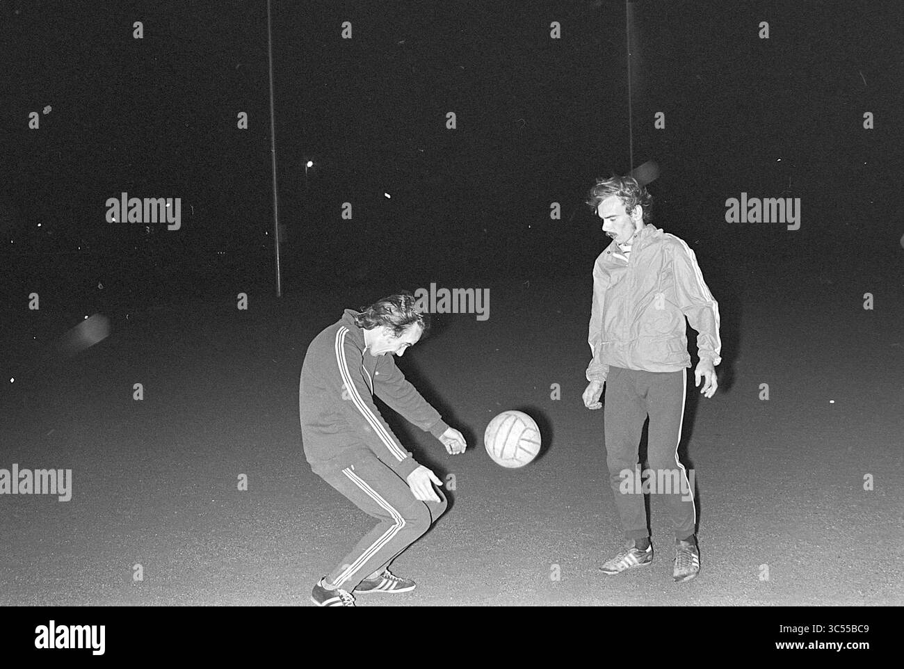 Due gemelli di calcio di Liere da: KIC Velsen Noord, Football People and Trainer, 25-09-1975 Whizgle News, Dutch Desk, Paesi Bassi, 1950-2000 due uomini giocano a calcio sotto il cielo notturno, uno giocando abilmente la palla mentre l'altro guarda con attenzione. La scena cattura un momento di cameratismo e divertimento in un ambiente all'aperto. Foto Stock