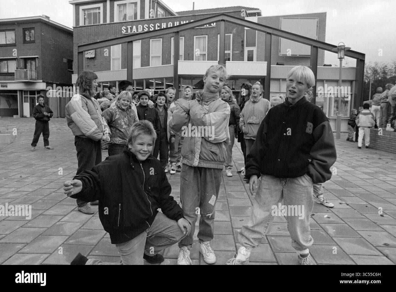 I bambini vanno all'opera IJmuiden, IJmuiden, Paesi Bassi, 08-10-1990 Whizgle News, Dutch Desk, i Paesi Bassi, 1950-2000 Un gruppo di bambini posa giocosamente in una piazza della città, mostrando un mix di stili dalla fine degli anni '80 ai primi anni '90 Alcuni stanno facendo espressioni divertenti, mentre altri sono riuniti sullo sfondo, creando un'atmosfera vivace piena di energia giovanile e cameratismo. Foto Stock