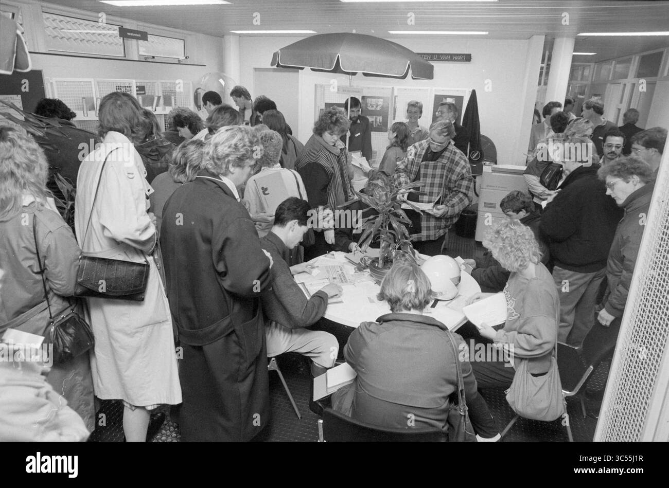 Job Market Lisse, Market, Lisse, 09-11-1986 Whizgle News, Dutch Desk, i Paesi Bassi, 1950-2000 Una folla di persone si riunisce intorno ai tavoli in un ambiente interno affollato, impegnato in conversazioni e attività. Alcune persone sono sedute, mentre altre si trovano nelle vicinanze, creando un'atmosfera di eccitazione e coinvolgimento. Vari elementi e documenti sono visibili sui tavoli, suggerendo un evento organizzato o un raduno. Foto Stock