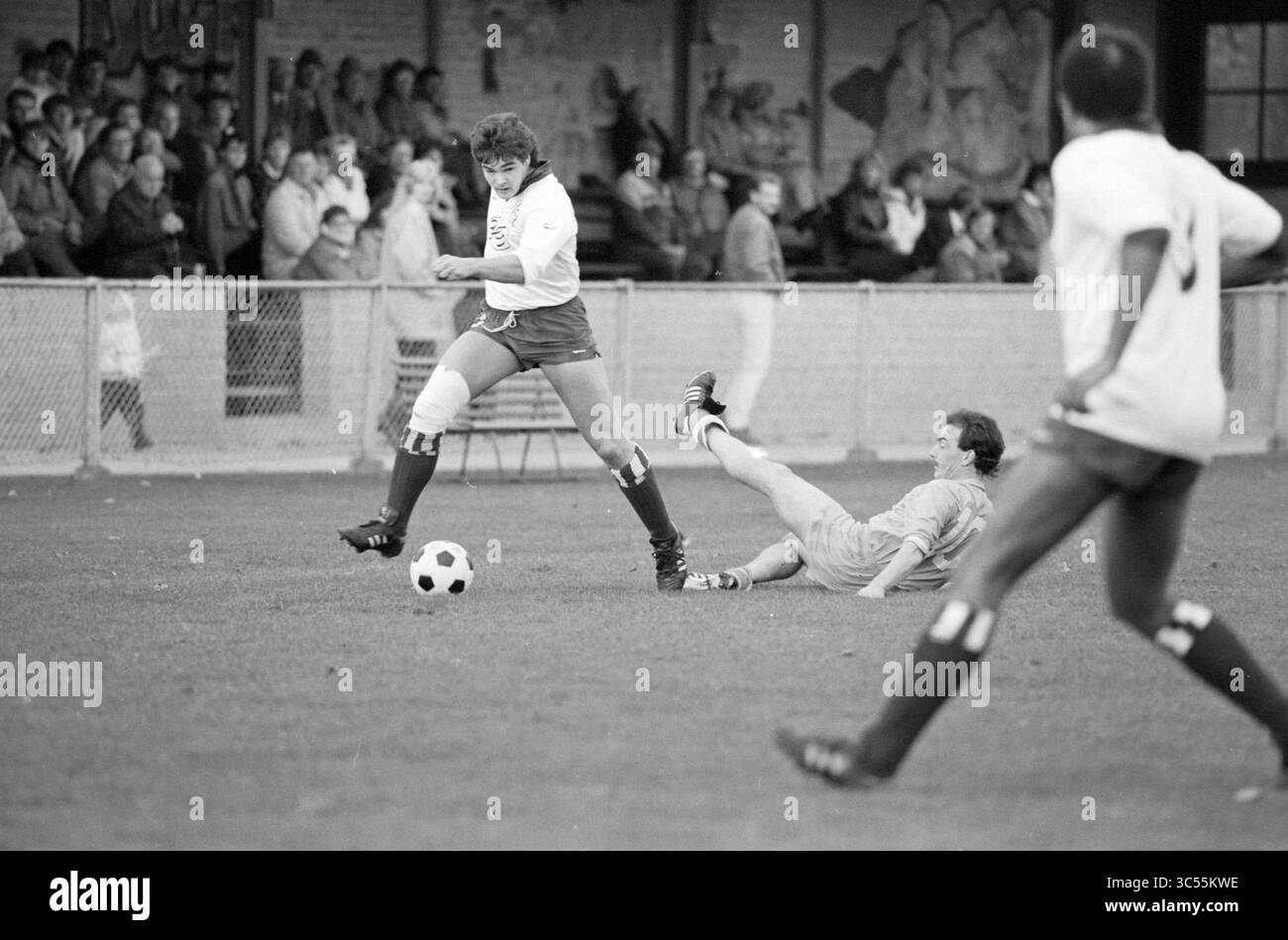 Partita di calcio Kon. HFC, 00-11-1986 Whizgle News, Dutch Desk, Paesi Bassi, 1950-2000 Un calciatore evade abilmente Un placcaggio mentre un altro giocatore si allunga per terra, tentando di fare una partita. La scena cattura l'intensità del gioco, con gli spettatori sullo sfondo che guardano da vicino. Foto Stock