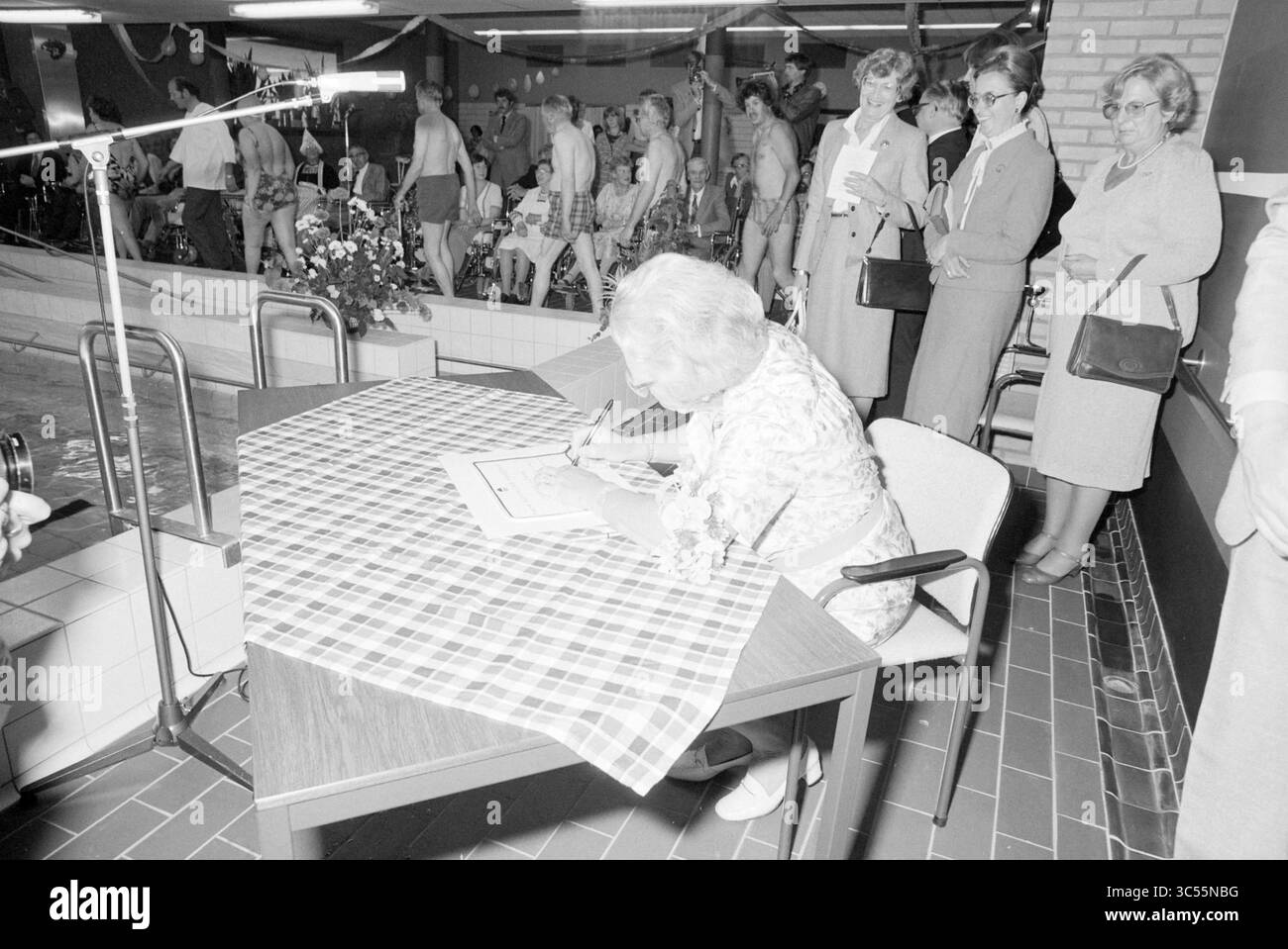 Princess Juliana apre la piscina, Heliomare Wijk aan Zee, ricevimenti reali e visite reali, Wijk aan Zee, 19-05-1981 Whizgle News, Dutch Desk, Paesi Bassi, 1950-2000 una donna anziana si siede a un tavolo, concentrata sul disegno o sulla scrittura, mentre una folla di spettatori osserva da una vicina area piscina. L'atmosfera e' vivace, con persone che si godono varie attivita' e si impegnano in conversazione. Foto Stock