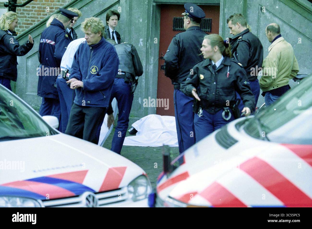 Suicide City Hall, Haarlem, Paesi Bassi, 21-11-2001 Whizgle News, Dutch Desk, i Paesi Bassi, 1950-2000 Un gruppo di agenti di polizia è riunito vicino a un'entrata, per assistere a una scena in cui una figura coperta giace a terra. Diversi veicoli sono parcheggiati nelle vicinanze, e gli agenti sono impegnati in varie attività legate alle indagini. Foto Stock
