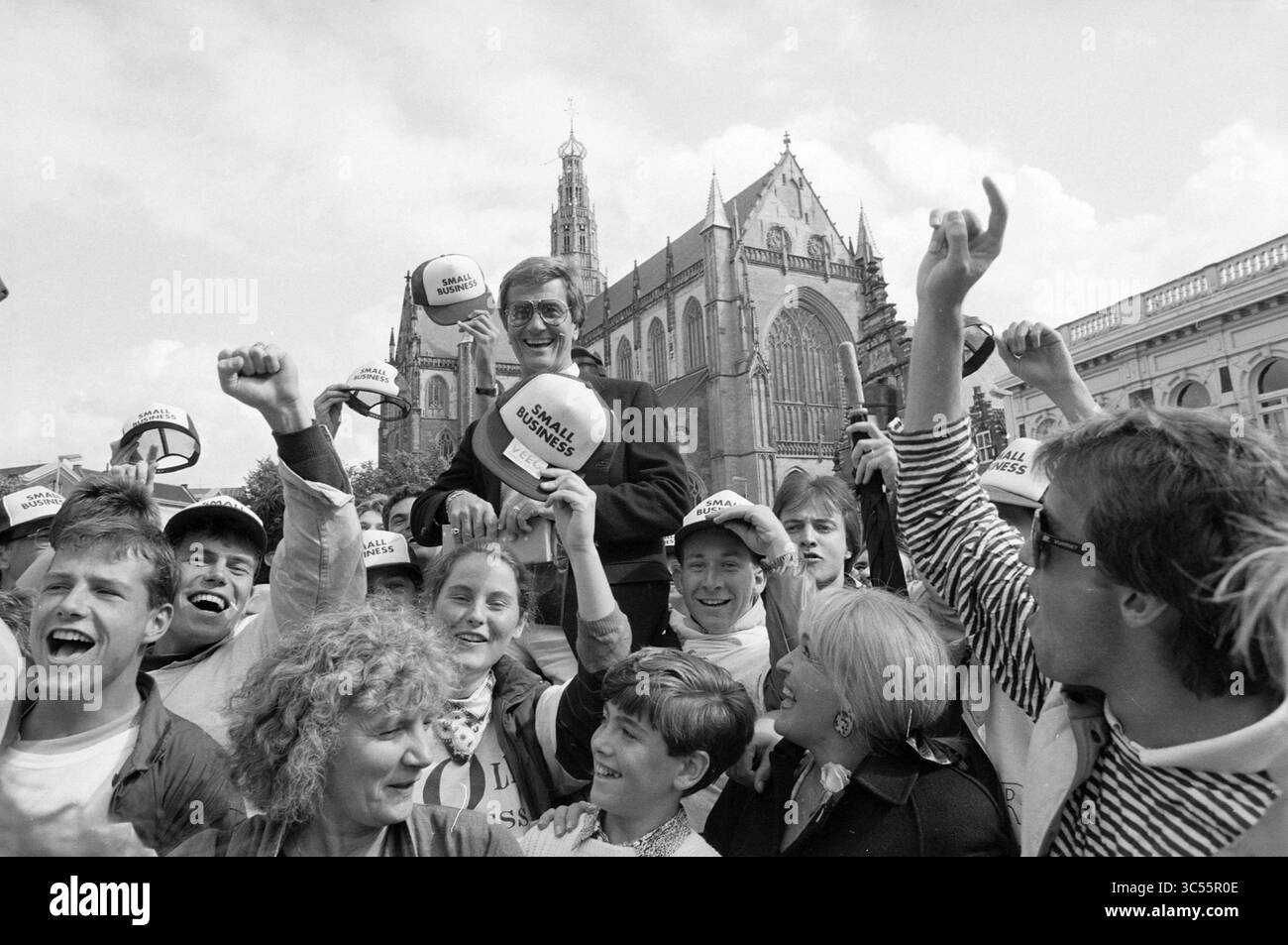 Pat Boone in the Grote Kerk e Grote Markt, Singing, Haarlem, Grote Markt, Paesi Bassi, 02-09-1988 Whizgle News, Dutch Desk, Paesi Bassi, 1950-2000 Una folla giubilante celebra, alzando le mani in gioia indossando cappelli impreziositi da uno slogan. Nel centro, un leader travolgente viene issato sulle spalle, trasudando entusiasmo in mezzo all'architettura storica sullo sfondo. Foto Stock