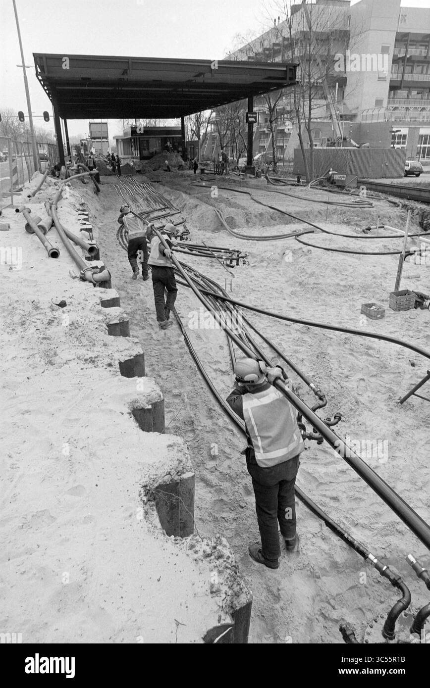 Renovation esso PUMP, Schipholweg, Schipholweg, 23-03-1995 Whizgle News, Dutch Desk, i Paesi Bassi, 1950-2000 lavoratori sono impegnati in un progetto di costruzione, che prevede lunghe tubature lungo una zona sabbiosa. Gli alberi e gli edifici urbani sono visibili sullo sfondo, con attrezzature e segnali stradali che indicano un sito di lavoro attivo. L'equipaggiamento di sicurezza, inclusi caschi e giubbotti riflettenti, viene indossato dall'equipaggio durante la manovra dei materiali idraulici. Foto Stock