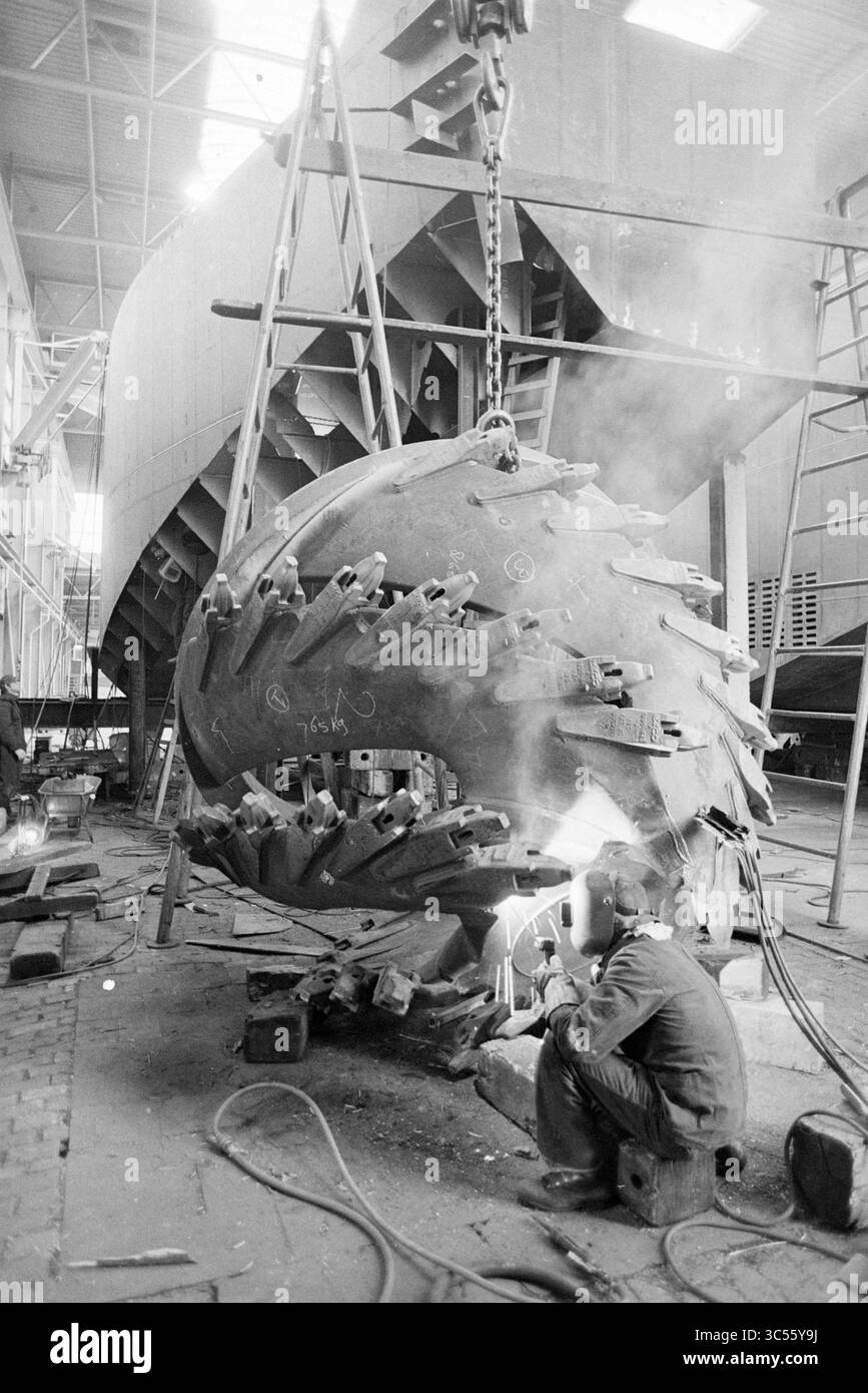 Cantiere Stapel Spaarndam, Spaarndam, Ships, 15-11-1978 Whizgle News, Dutch Desk, i Paesi Bassi, 1950-2000 Anni Un lavoratore salda meticolosamente una grande e complessa componente di macchinari in un ambiente di costruzione, circondato da impalcature e attrezzature pesanti sullo sfondo, mentre dalla torcia di saldatura fuoriesce un pennacchio di fumo. Foto Stock