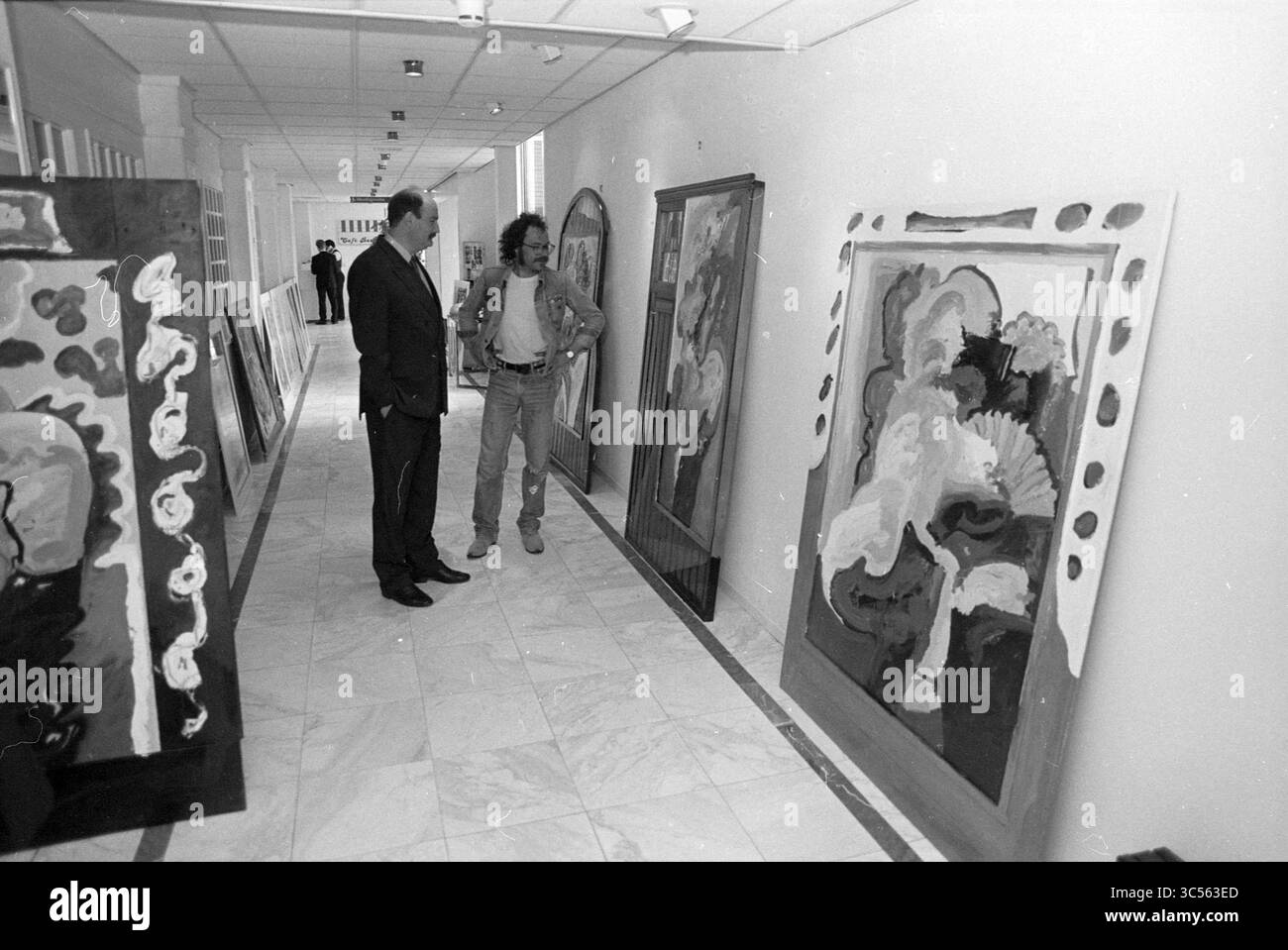 Decorazione della mostra Golden Tulip, 09-05-1990 Whizgle News, Dutch Desk, Paesi Bassi, 1950-2000 due persone si trovano in un corridoio, impegnati in conversazione mentre osservano diversi grandi e colorati dipinti astratti esposti lungo le pareti. L'atmosfera suggerisce un focus sull'apprezzamento dell'arte e la discussione. Foto Stock