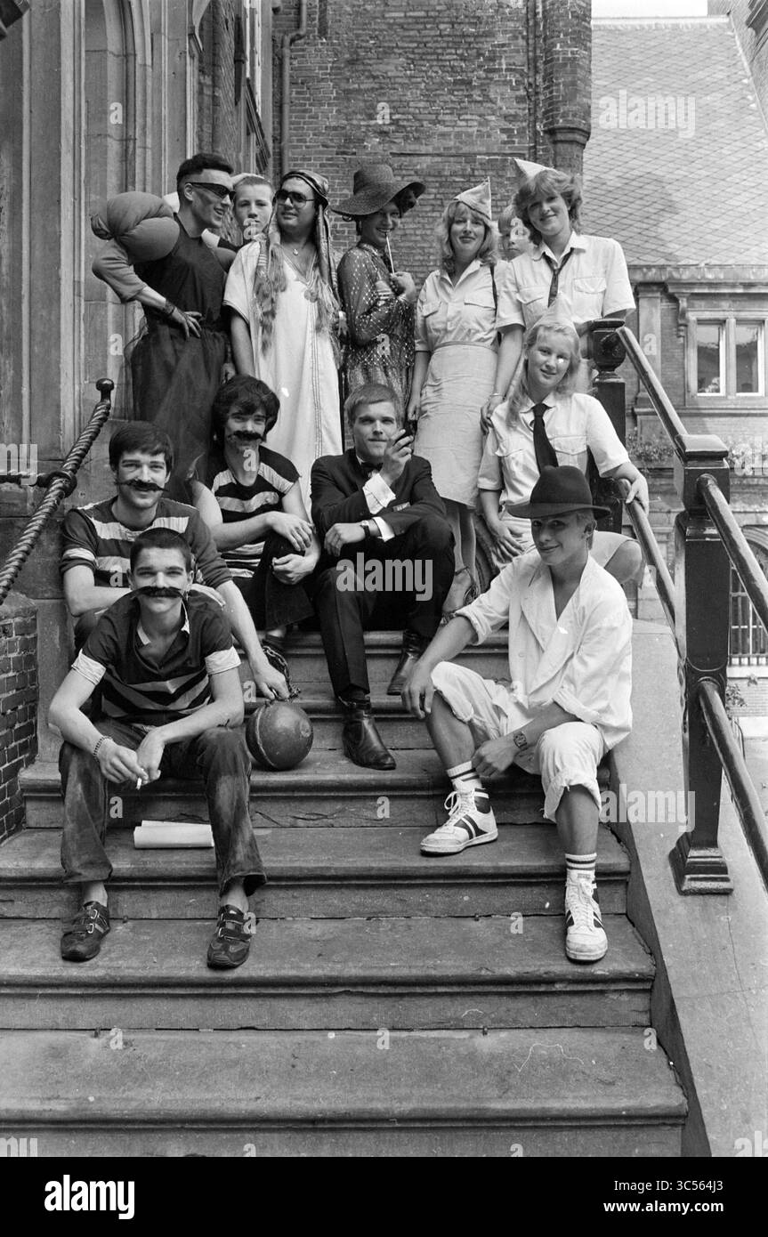 Gruppo di giovani vestiti da personaggi famosi, gruppi, abbigliamento, 06-08-1983 Whizgle News, Dutch Desk, paesi Bassi, 1950-2000 Un gruppo eterogeneo di individui posa giocosamente su una serie di scale, mostrando un mix di stili ed espressioni. Alcune sono vestite con abbigliamento casual, mentre altre sfoggiano abiti più formali o stravaganti. L'atmosfera è allegra e rilassata, mettendo in risalto il cameratismo del gruppo. Foto Stock