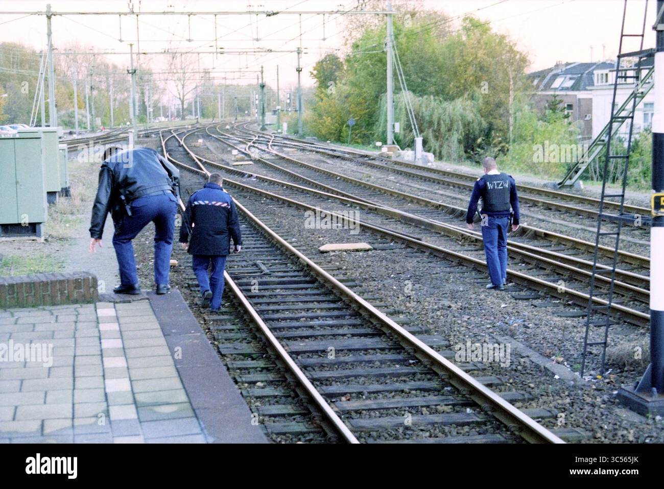 Sparatutto alla stazione di Haarlem, Haarlem, Paesi Bassi, 14-11-1999 Whizgle News, Dutch Desk, i Paesi Bassi, 1950-2000 due persone in uniforme stanno ispezionando i binari ferroviari, uno accovacciato mentre perlustrano la zona. Attorno a loro si trovano diverse linee ferroviarie che si estendono in lontananza, con vegetazione e strutture visibili lungo i lati. Foto Stock