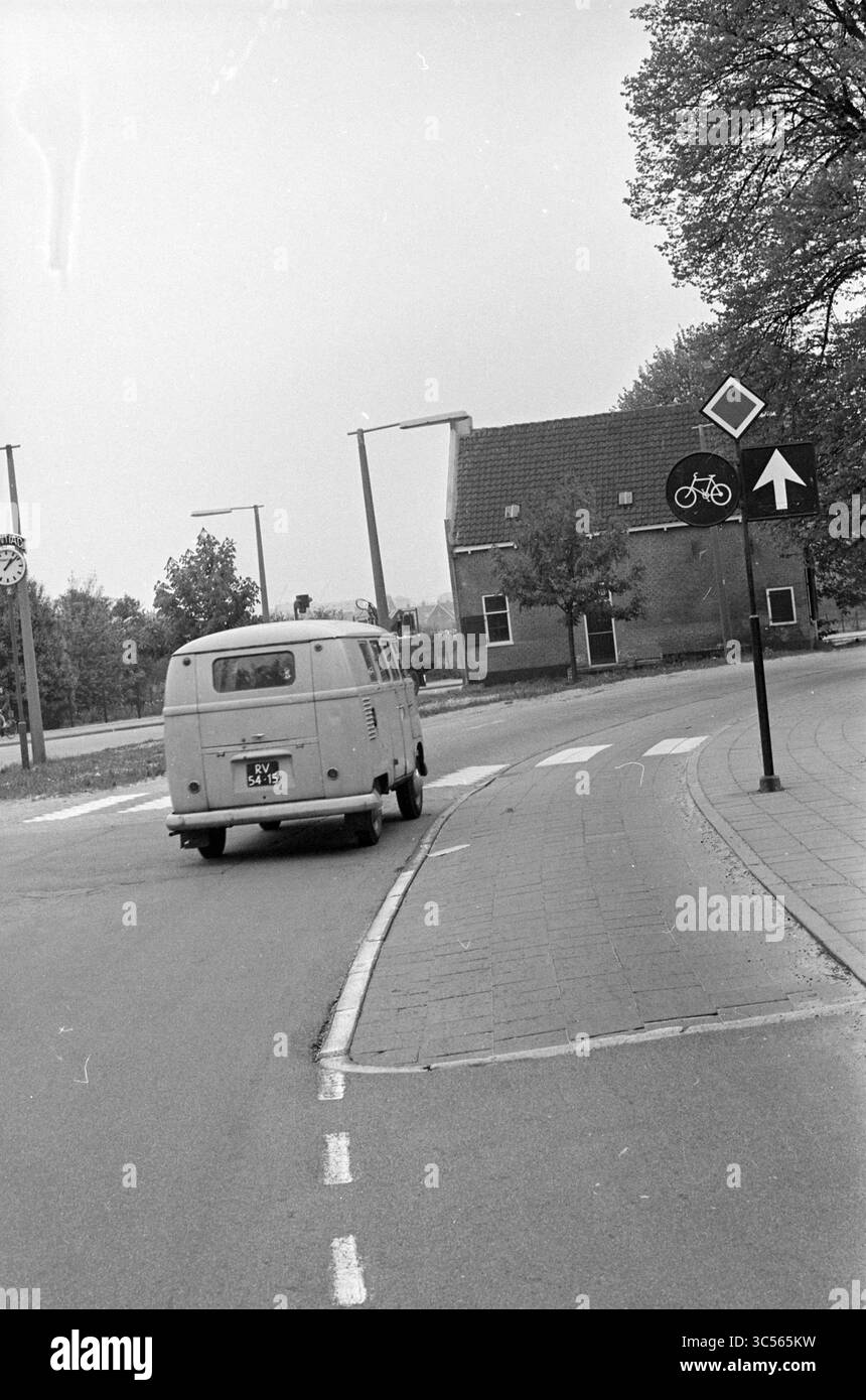 Via con VW van Whizgle News, Dutch Desk, Paesi Bassi, 1950-2000 Un furgone d'epoca fa una svolta su una strada tranquilla, passando davanti a una casa con un tetto caratteristico. Nelle vicinanze, un cartello con la pista ciclabile conduce i ciclisti, circondati da alberi che suggeriscono un paesaggio sereno. Foto Stock
