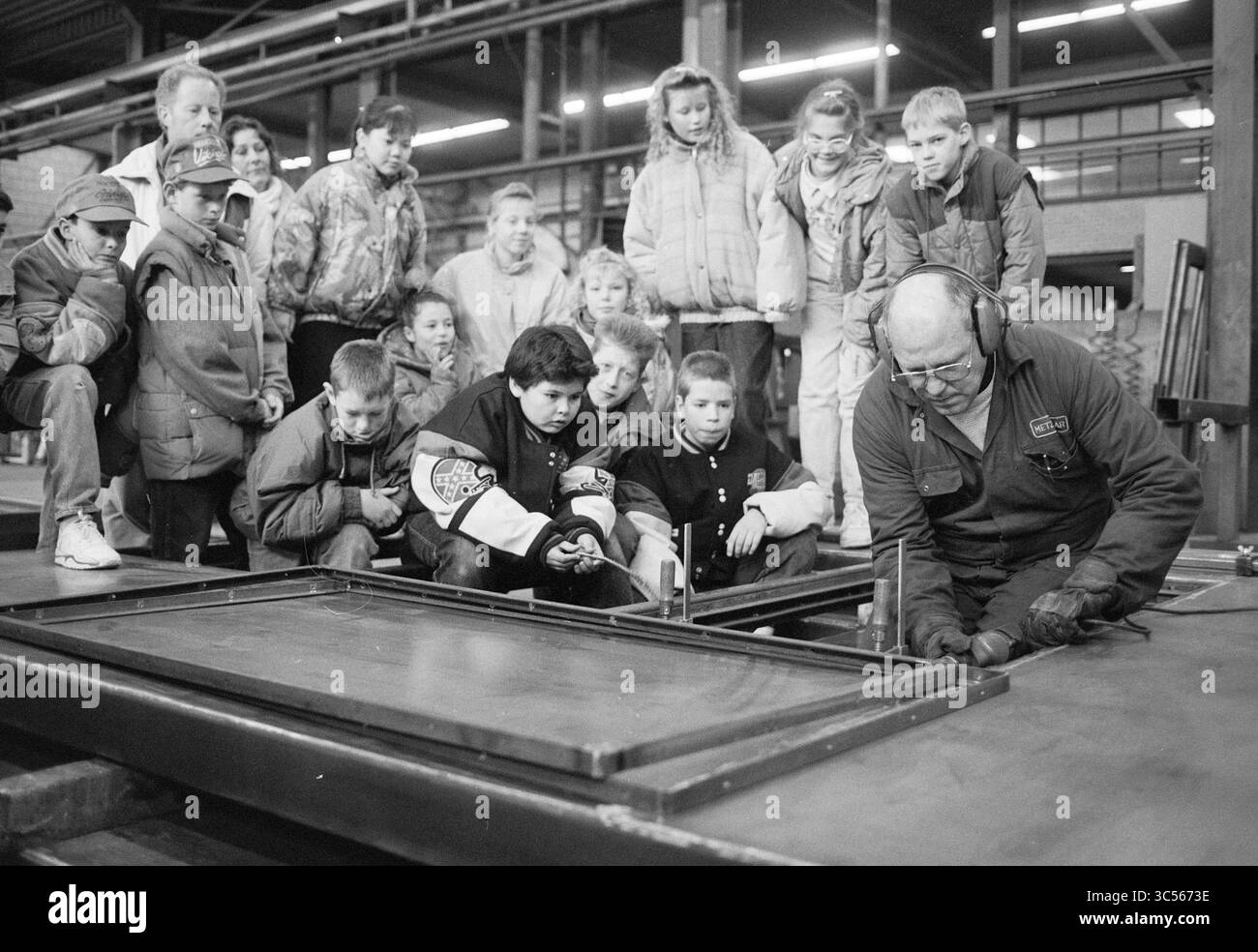 School de Dennekop at Metzelaar, IJmuiden, IJmuiden, Paesi Bassi, 04-02-1991 Whizgle News, Dutch Desk, Paesi Bassi, 1950-2000 Un gruppo di bambini guarda con attenzione come un lavoratore qualificato dimostra una tecnica di lavorazione dei metalli, evidenziando un momento di apprendimento e curiosità in un ambiente industriale. Foto Stock