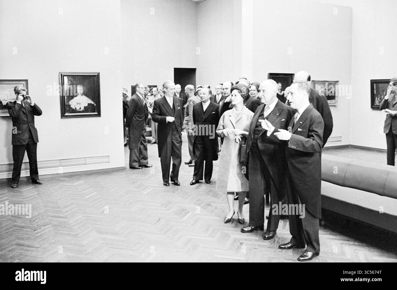 Visita al Rijksmuseum di Amsterdam durante la visita di stato del presidente austriaco A. Schärf in compagnia, tra gli altri, della regina Giuliana, del principe Bernhard e del sindaco G. van Hall di Amsterdam, Amsterdam, Paesi Bassi, 16-05-1961 Whizgle News, Dutch Desk, i Paesi Bassi, 1950-2000 Un gruppo di individui elegantemente vestiti, tra cui figure di rilievo, stanno osservando attentamente le opere d'arte in una galleria. Alcuni sono impegnati nella conversazione, mentre altri prendono appunti o foto, mostrando una miscela di curiosità e ammirazione per i pezzi esposti. Foto Stock