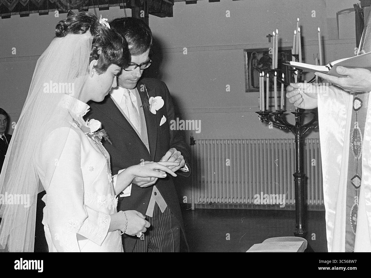 Marriage Peter Heemskerk, Marriage, 14-05-1970 Whizgle News, Dutch Desk, Paesi Bassi, 1950-2000 Una sposa e uno sposo si scambiano le nozze durante una cerimonia, circondati da un'atmosfera serena. La sposa, decorata con un abito elegante e un velo, guarda con amore la sua compagna, vestita con un abito classico. Le candele sfarfallio sullo sfondo, aggiungendo calore al momento. Foto Stock