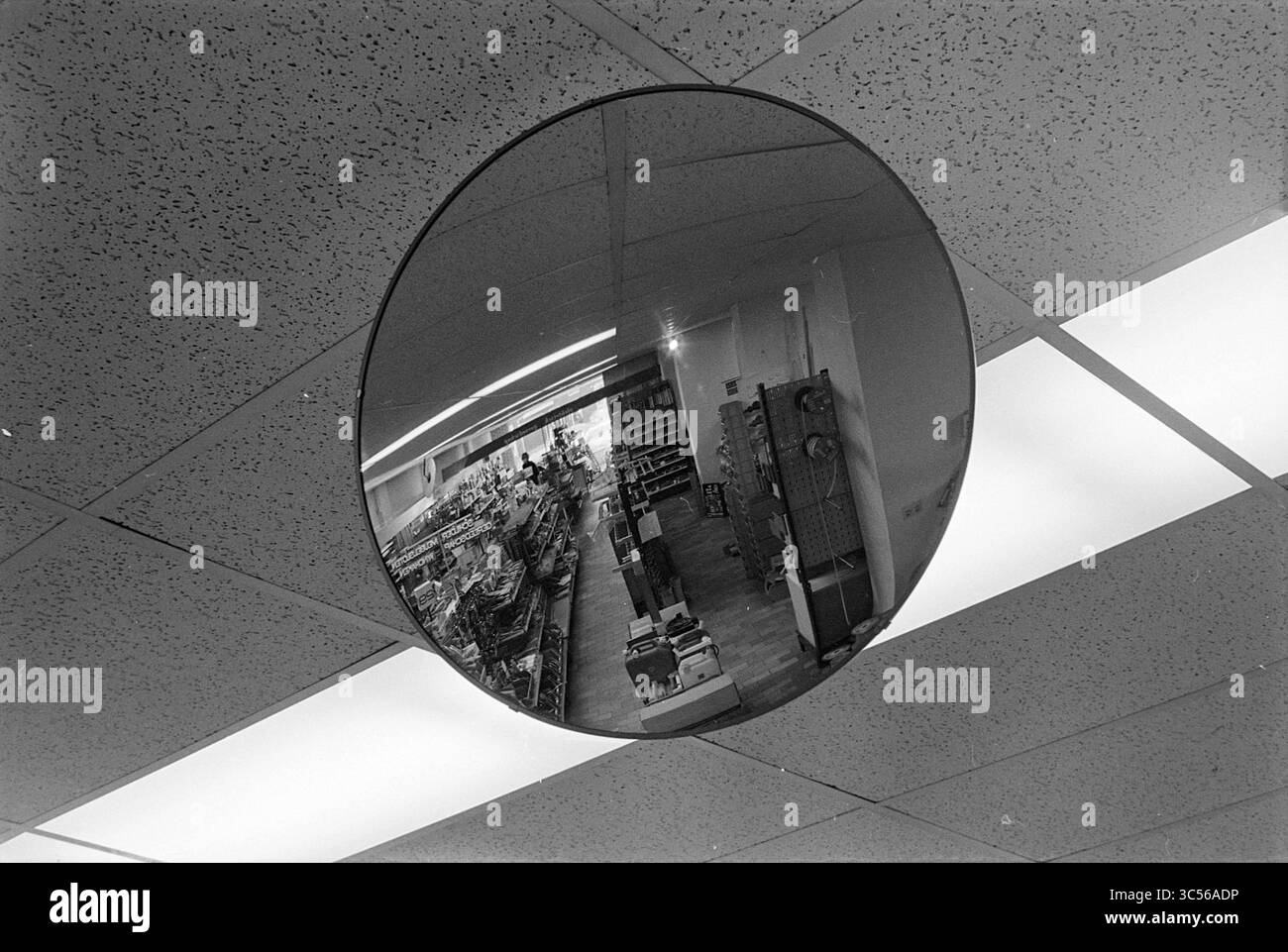 Specchio interno, occhiali con lenti per specchio, specchi, 10-12-1976 Whizgle News, Dutch Desk, Paesi Bassi, 1950-2000 Uno specchio convesso è appeso al soffitto, riflettendo un vivace corridoio di alimentari pieno di scaffali di vari prodotti e acquirenti che si occupano della loro attività. La superficie curva crea una vista distorta della scenografia sottostante. Foto Stock