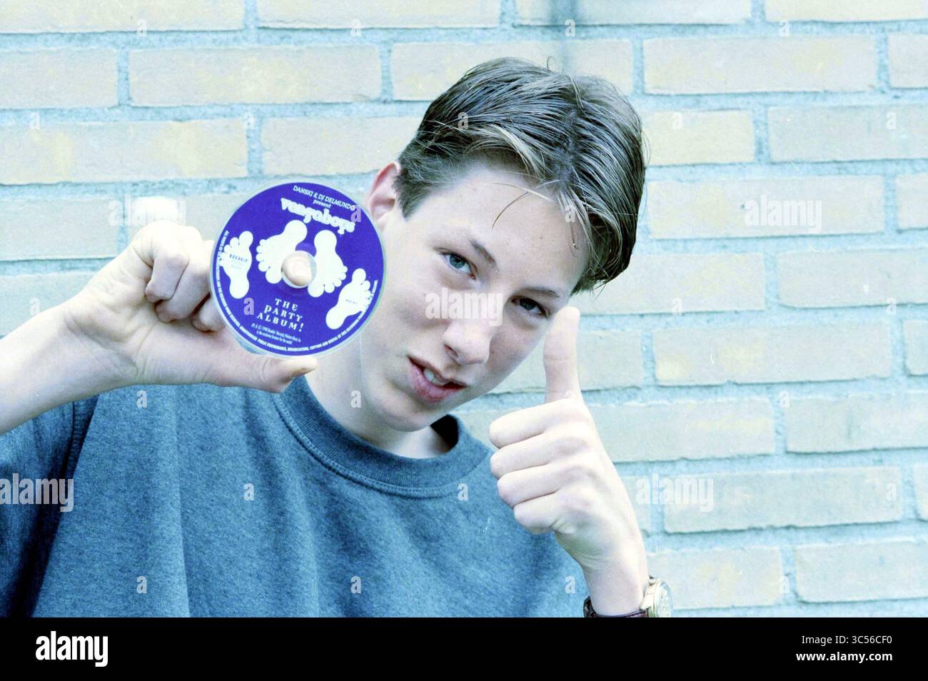 Coen van Boekel con CD, 02-07-1998 Whizgle News, Dutch Desk, Paesi Bassi, 1950-2000 Un giovane regge un disco rotondo mentre regge un pollice, mostrando entusiasmo. Lo sfondo presenta una parete testurizzata. Foto Stock