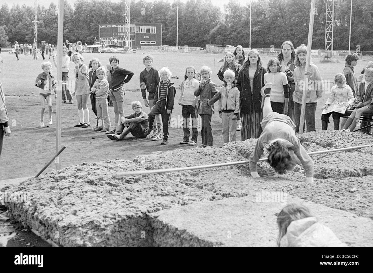 Bevertjesfeest, Beverwijk, Speliade in the Mel, Festival, feste e manifestazioni, 03-08-1972 Whizgle News, Dutch Desk, i Paesi Bassi, 1950-2000 Un gruppo di spettatori, tra cui bambini e adulti, si riuniscono intorno a un lungo pozzo per saltare in un evento sportivo all'aperto. Molti guardano con attenzione mentre un partecipante si prepara per un salto, mentre altri sono seduti o in piedi in gruppi, godendo l'atmosfera. Lo sfondo presenta un campo sportivo e alberi distanti, che si aggiungono alla vivace scena. Foto Stock