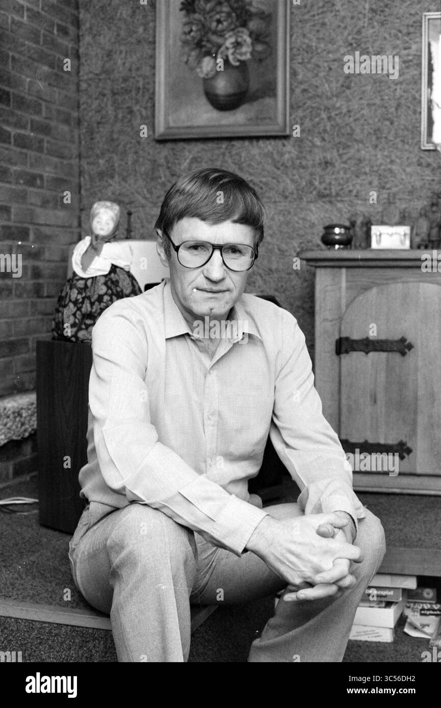 Uomo ritratto, 00-10-1988 Whizgle News, Dutch Desk, Paesi Bassi, 1950-2000 Un uomo con occhiali si siede casualmente su un pavimento, rivestito con camicia e pantaloni di colore chiaro. Ha un'espressione seria e riposa le mani insieme mentre è circondato da un interno accogliente con un armadio in legno, oggetti decorativi e un dipinto floreale sulla parete. Foto Stock