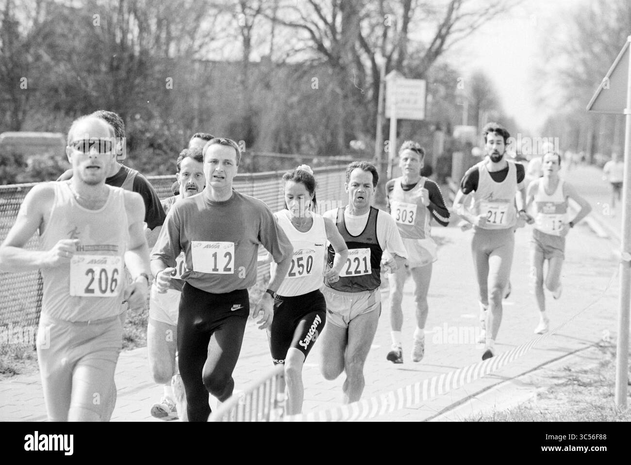Golden Tulip Run, Haarlemmermeer, 26-03-1994 Whizgle News, Dutch Desk, Paesi Bassi, 1950-2000 Un gruppo di corridori determinati gareggia in una gara, mostrando un mix di concentrazione e sforzo mentre percorrono un percorso alberato. Ogni atleta indossa una maglia numerata, sottolineando lo spirito competitivo dell'evento. Foto Stock