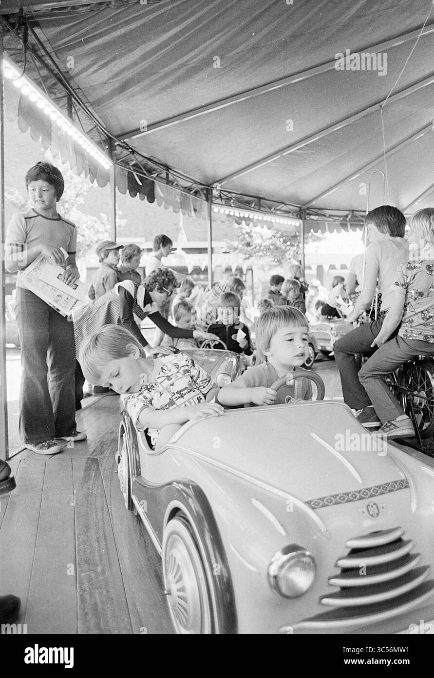 Mercato delle pulci Spaarnberg, Gate, Market, Santpoort-Zuid, Wüstelaan, 27-05-1977 Whizgle News, Dutch Desk, Paesi Bassi, 1950-2000 Una scena vivace cattura un gruppo di bambini che si divertono in una fiera colorata, con due giovani giocherelloni seduti in un'auto in miniatura mentre altri si dedicano a varie attività nelle vicinanze. Espressioni gioiose e interazioni giocose definiscono l'atmosfera, evocando un senso di spensieratezza nell'infanzia. Foto Stock