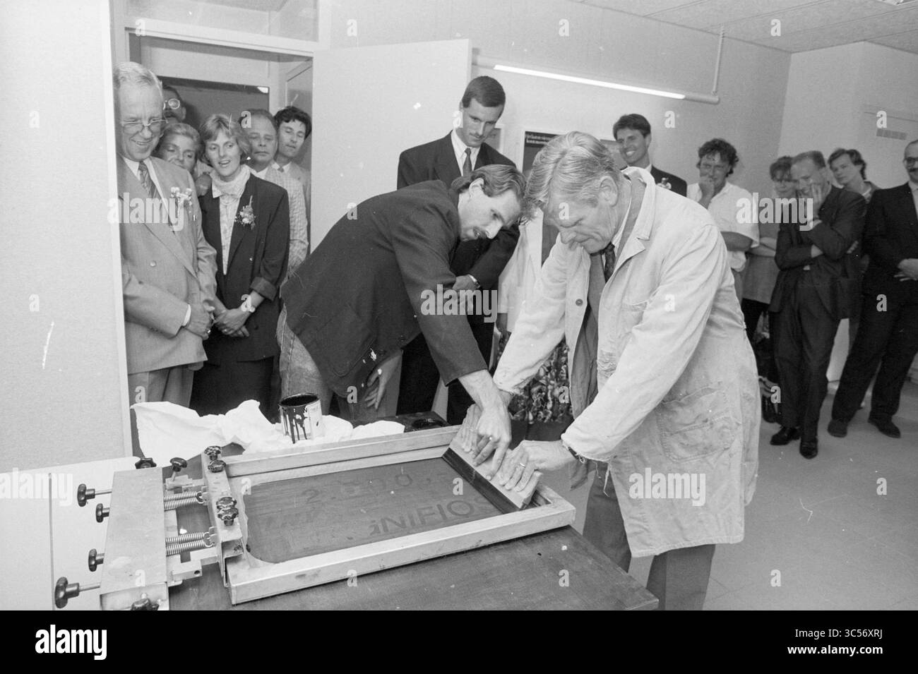 Apertura nw. Ufficio VSB Lisse, Nuts, United Savings Banks, 30-06-1989 Whizgle News, Dutch Desk, paesi Bassi, 1950-2000 Un gruppo di persone guarda attentamente come due persone lavorano a un progetto di serigrafia, applicando l'inchiostro su un grande schermo. L'atmosfera è piena di curiosità ed eccitazione mentre si preparano a svelare il design finito. Foto Stock
