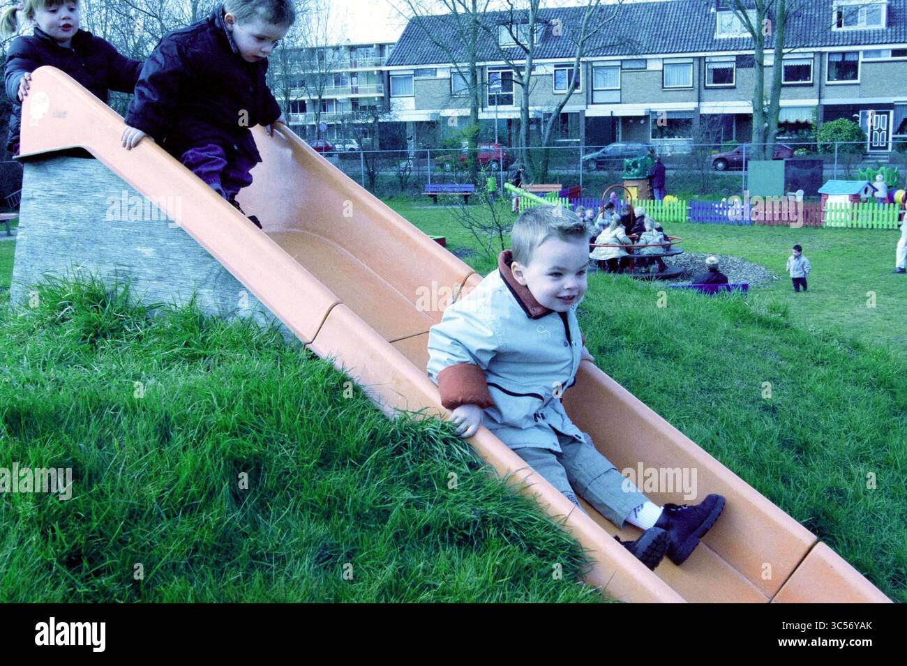 Apertura del parco giochi Orionweg IJmuiden, IJmuiden, Nederland, 23-03-2002 Whizgle News, Dutch Desk, nei Paesi Bassi, 1950-2000 bambini giocano con gioia su uno scivolo in un vivace parco giochi all'aperto, con un bambino che scivola giù mentre altri guardano e si impegnano in varie attività nelle vicinanze. La scena è piena di risate e l'energia della giocosità giovanile. Foto Stock