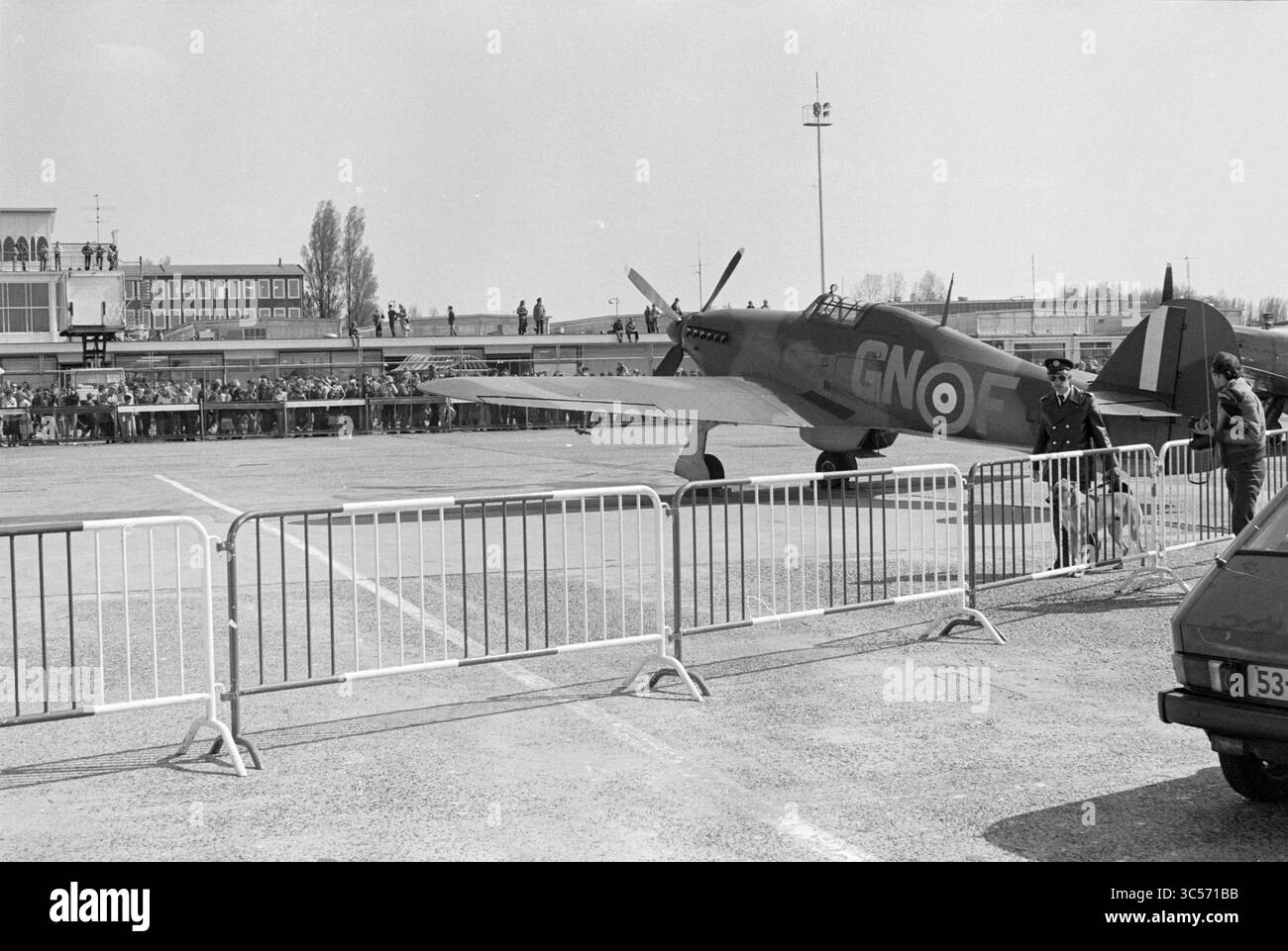 Mostra di aerei della seconda guerra mondiale, Schiphol, Schiphol, Schiphol, 05-05-1980 Whizgle News, Dutch Desk, Paesi Bassi, 1950-2000 Uno storico aereo da caccia, contrassegnato da insegne riconoscibili, è posizionato vicino a una barriera di folla su un campo di aviazione. Gli osservatori si riuniscono sullo sfondo, mostrando interesse per l'aereo, mentre alcune persone in uniforme mantengono l'ordine intorno alla scena. Foto Stock